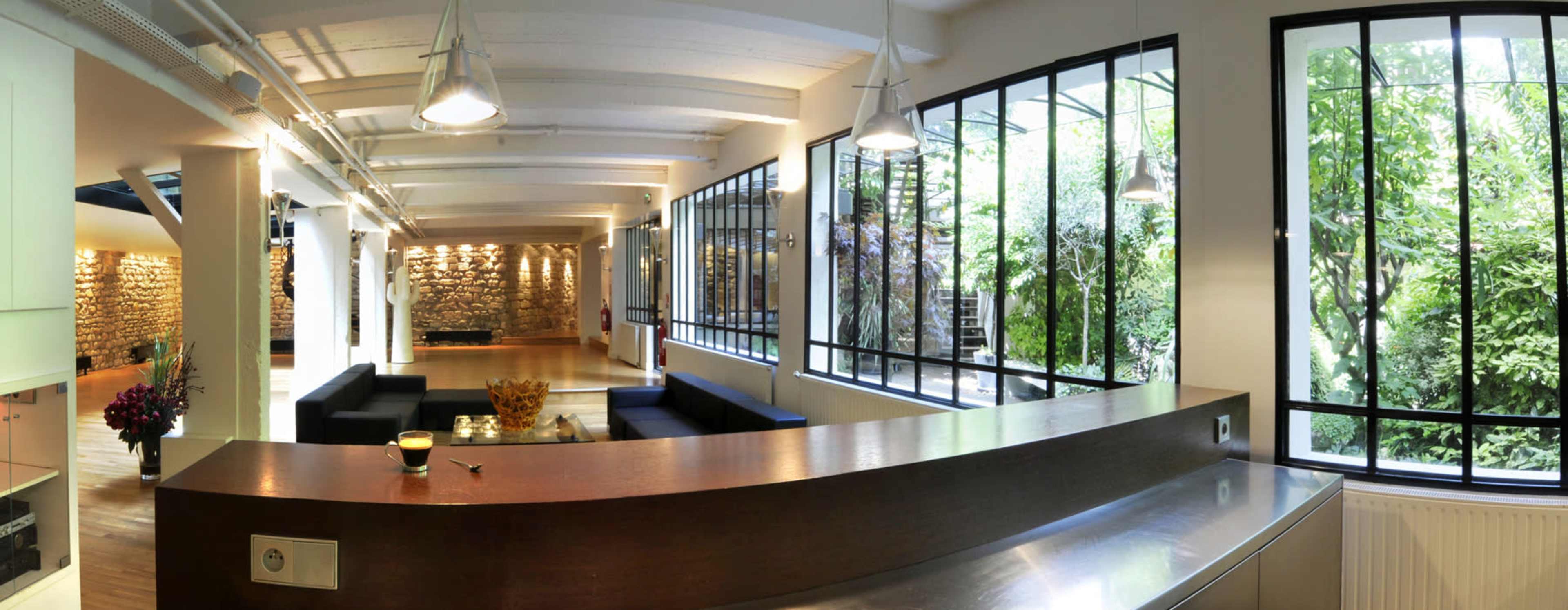 A modern, open-concept living space with large windows overlooking a garden, featuring a minimalist kitchen counter and comfortable seating areas.