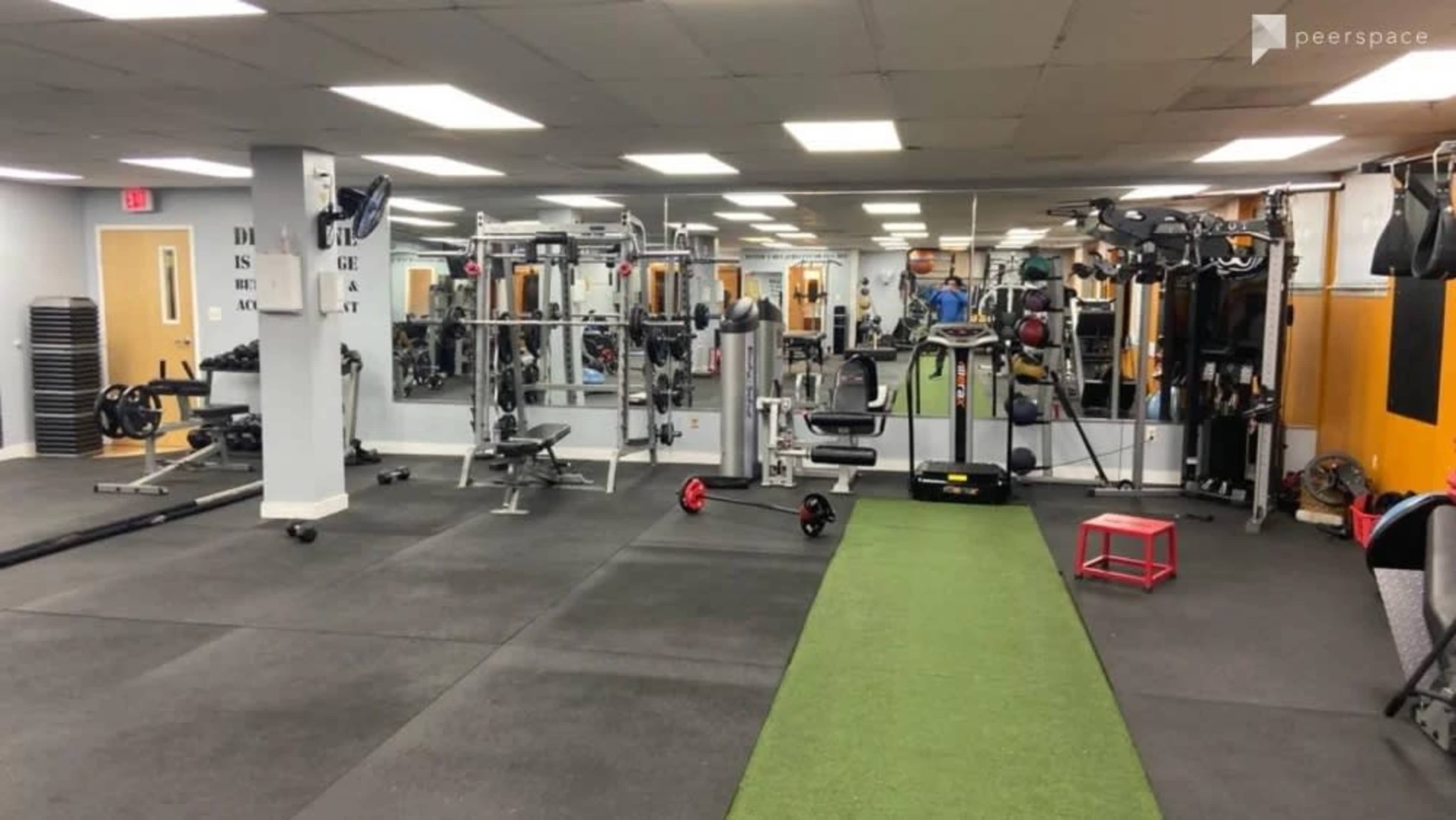 A gym featuring various fitness equipment, mirrors, and a green exercise mat on the floor.