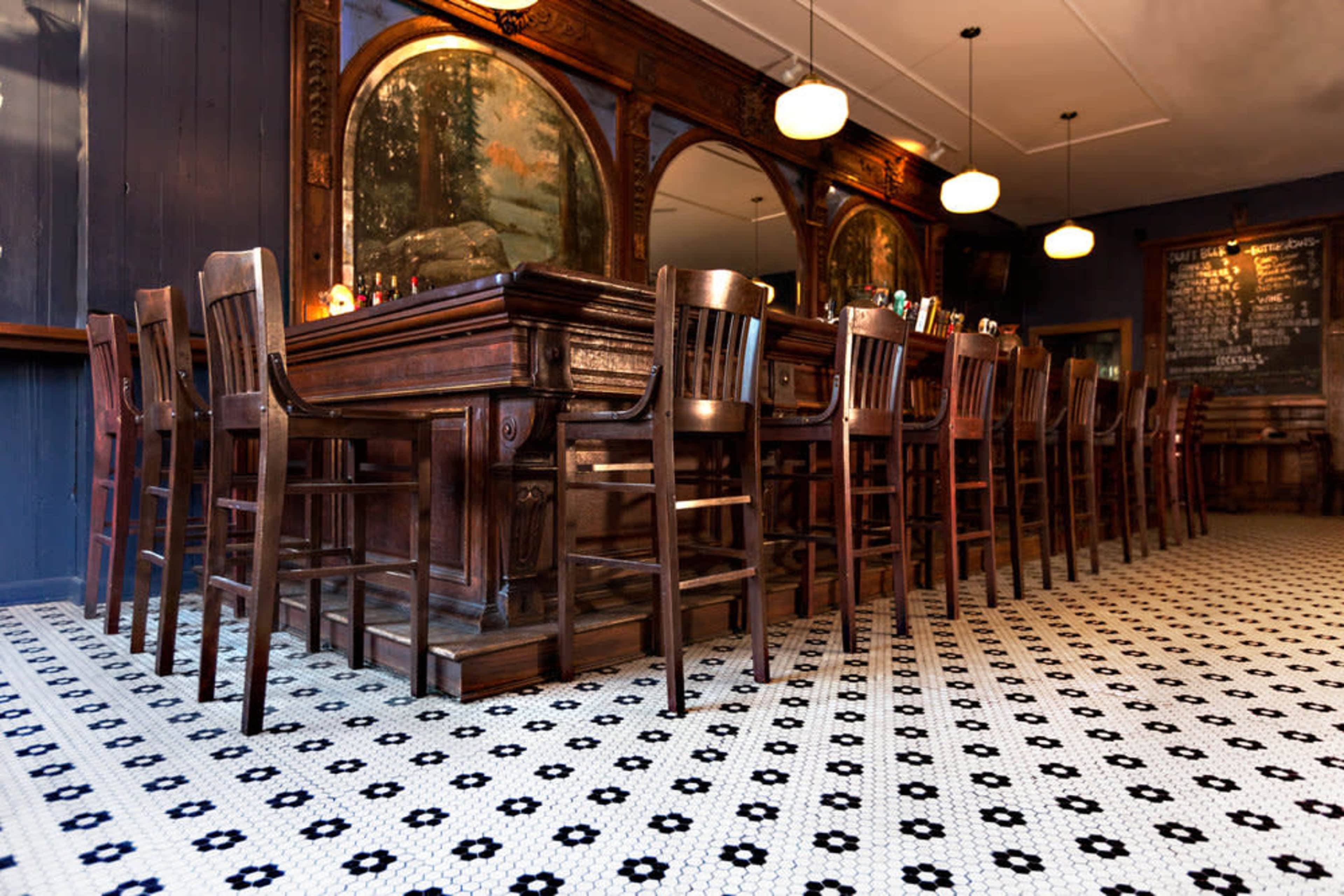 A dimly lit bar scene with a long wooden table surrounded by high-backed chairs and decorative mirrors on the walls.
