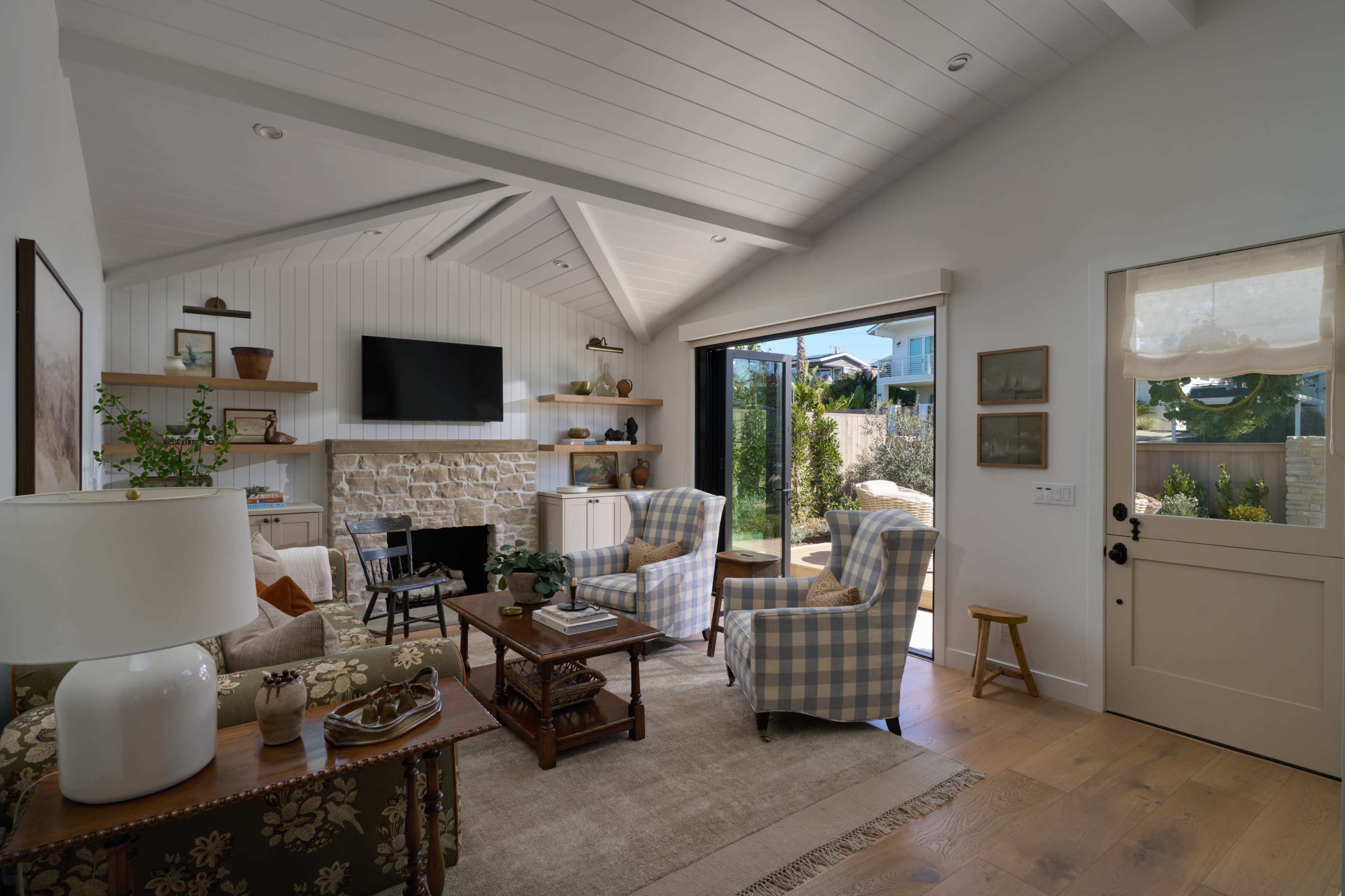 A bright living room with a stone fireplace, two checkered chairs, a wooden coffee table, and a sliding glass door leading to an outdoor area.