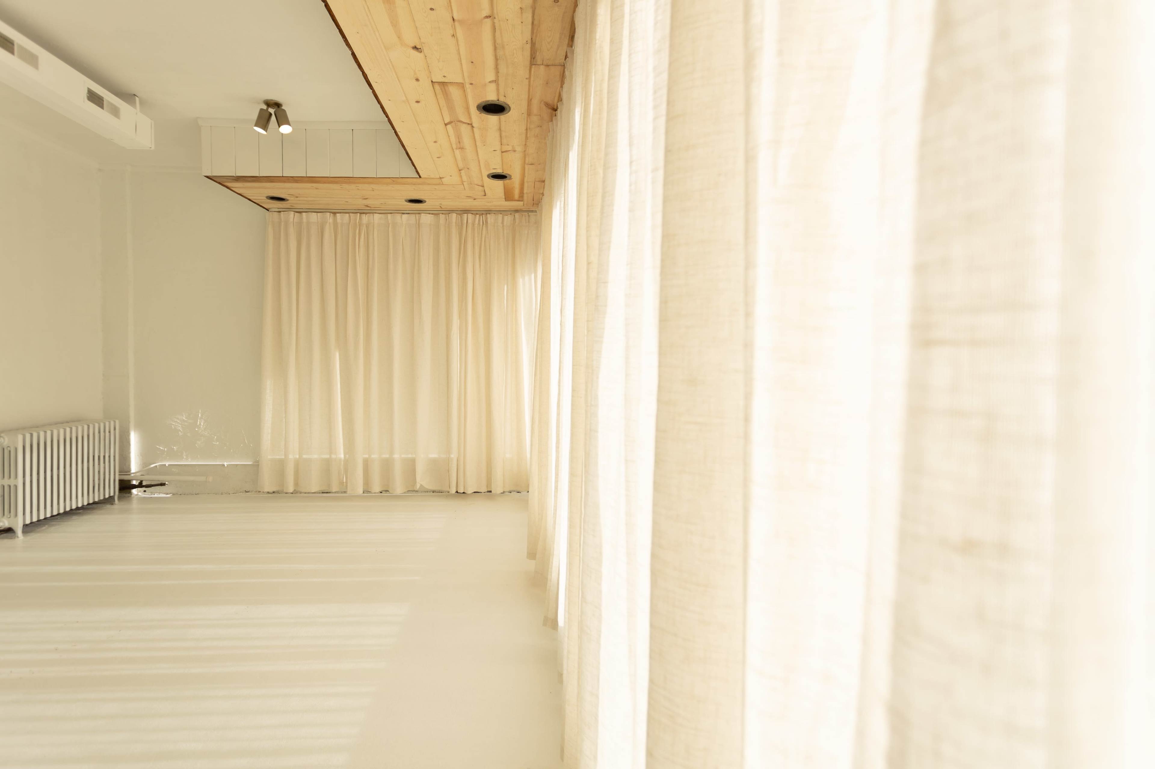 The image shows a bright, minimalist interior featuring sheer curtains and a wooden ceiling.