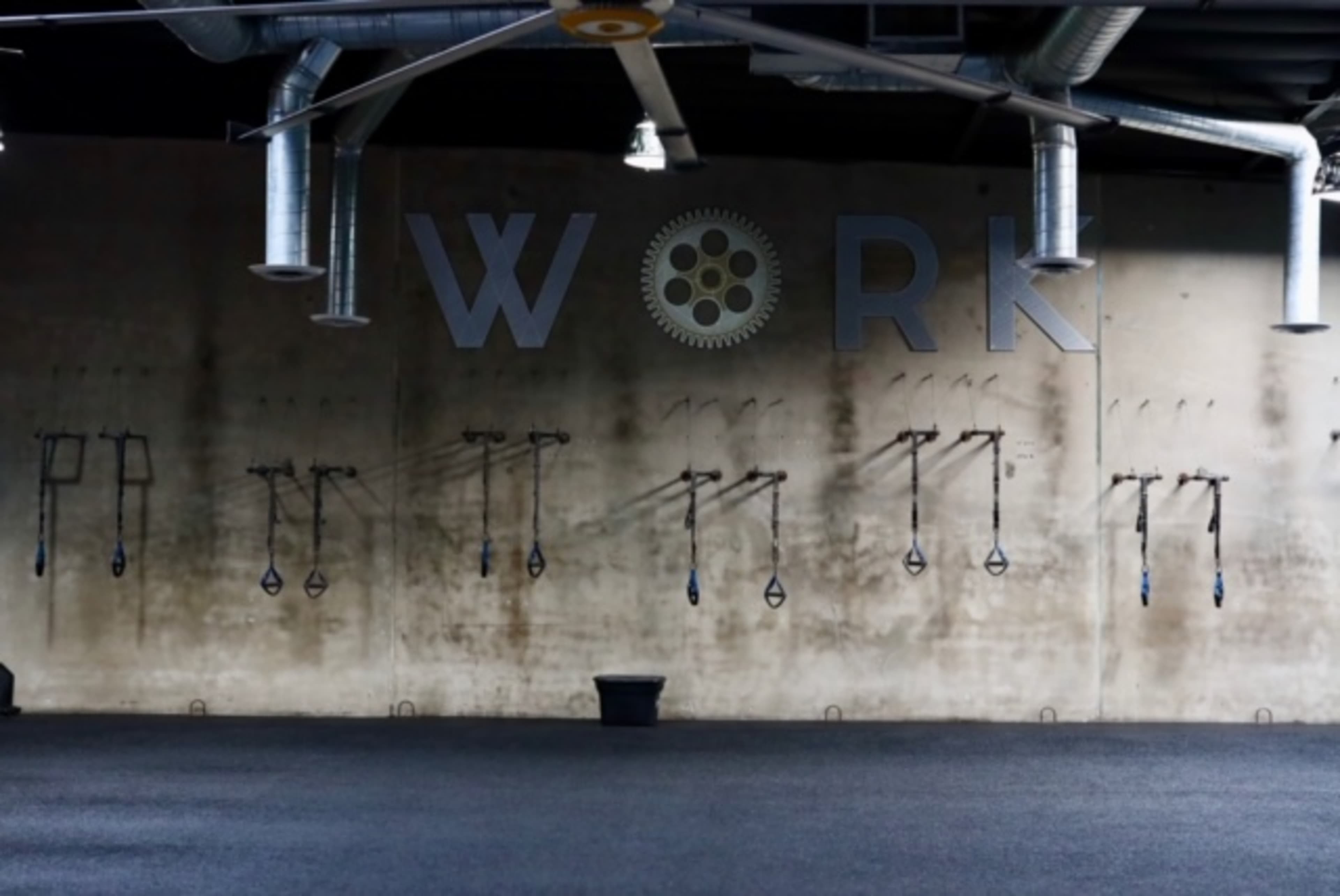 A gym interior with a wall displaying the word "WORK" and various exercise equipment hanging in organized rows.