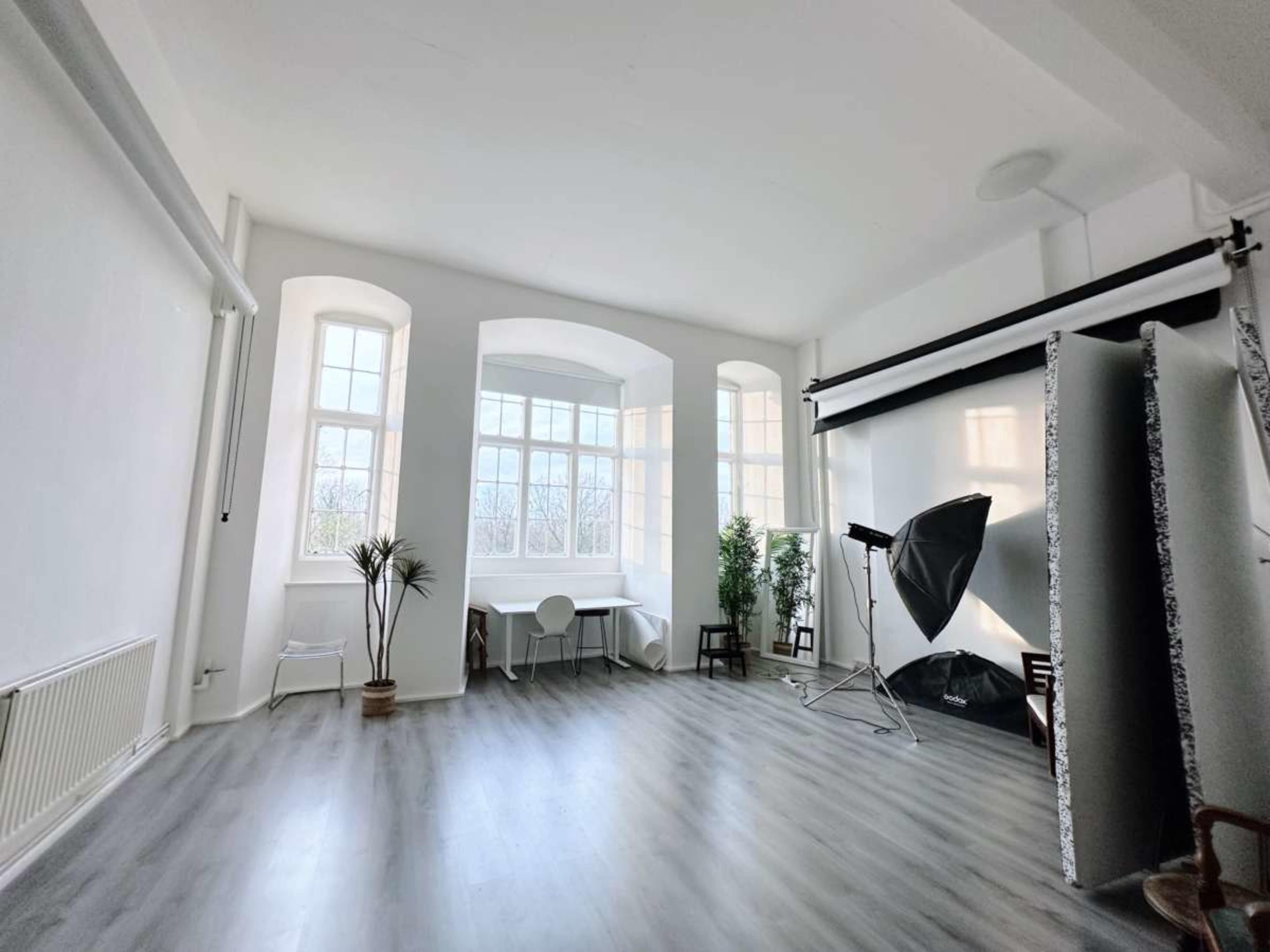 A spacious photography studio features large windows, a simple table setting, and a backdrop setup.