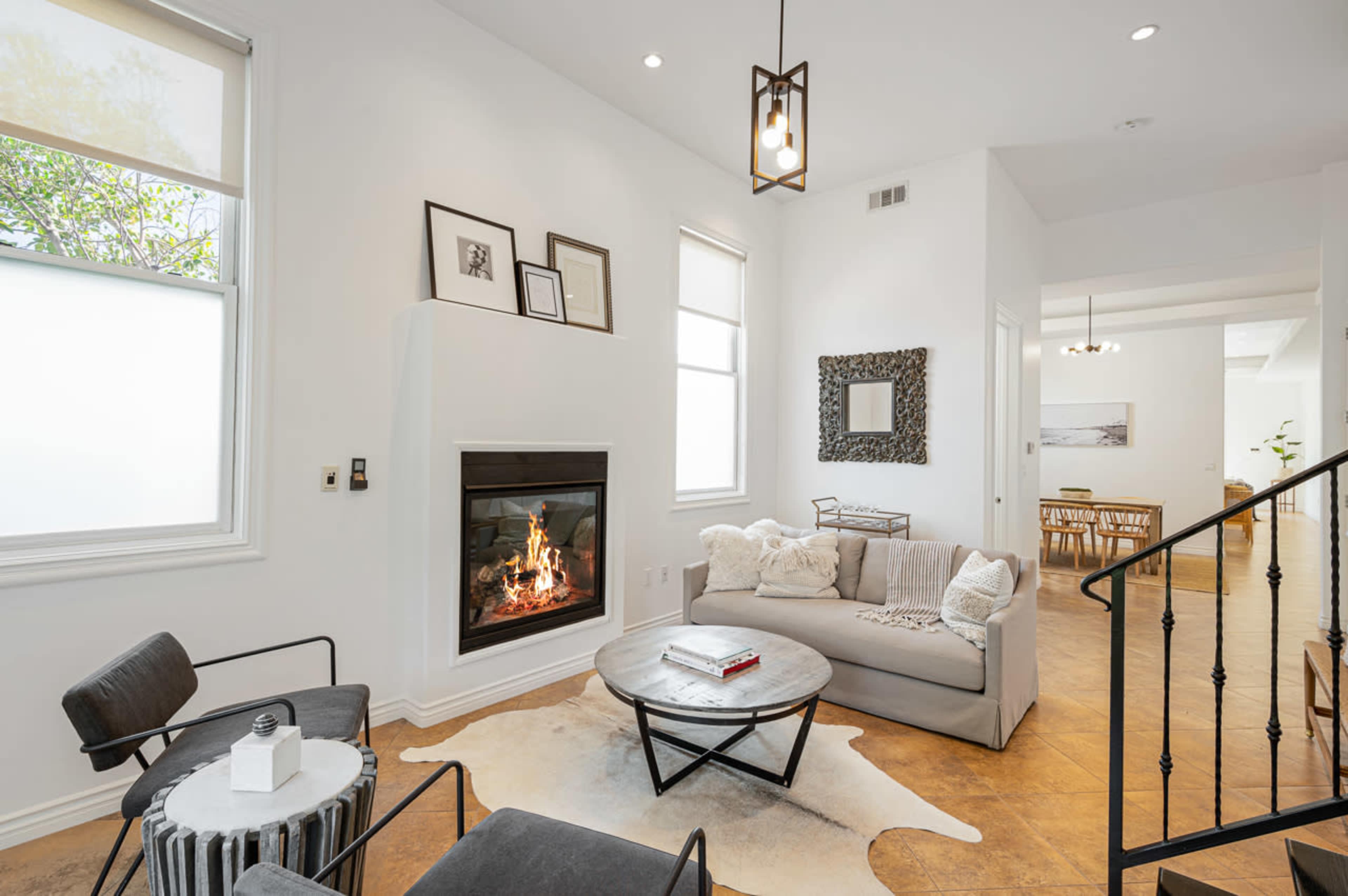 The bright living room features a modern sofa, a circular coffee table, and a cozy fireplace surrounded by framed artwork.