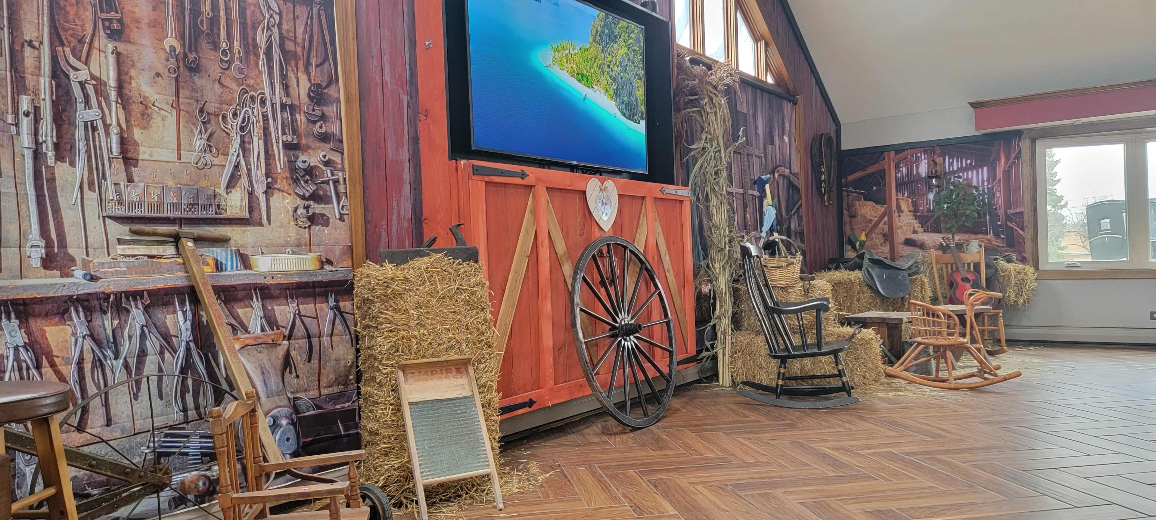 The scene features a rustic-themed interior with wooden furniture, hay bales, and a large screen displaying an island landscape.