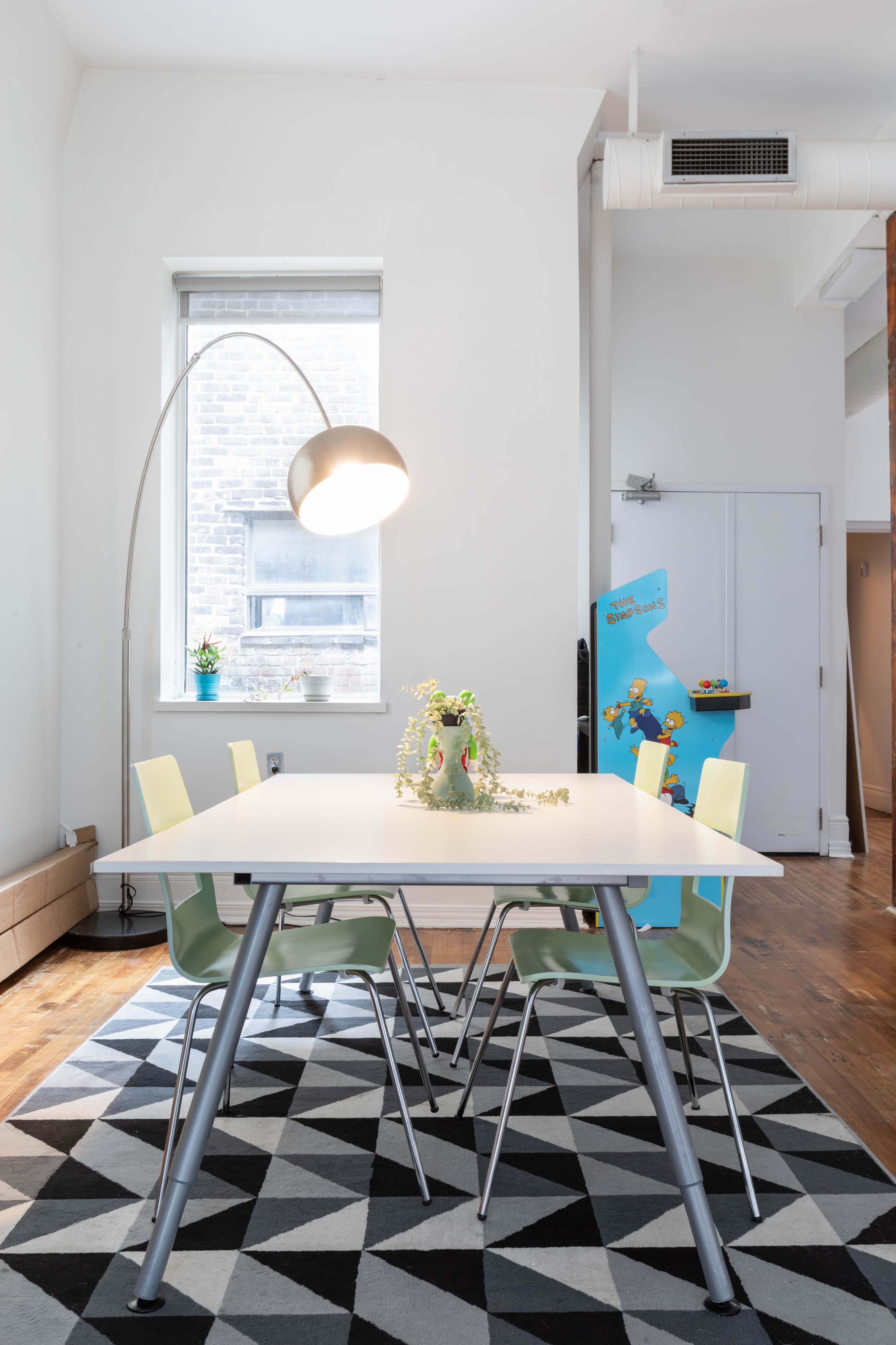 A modern dining area features a table surrounded by four chairs, with a floor lamp overhead and a patterned rug beneath.