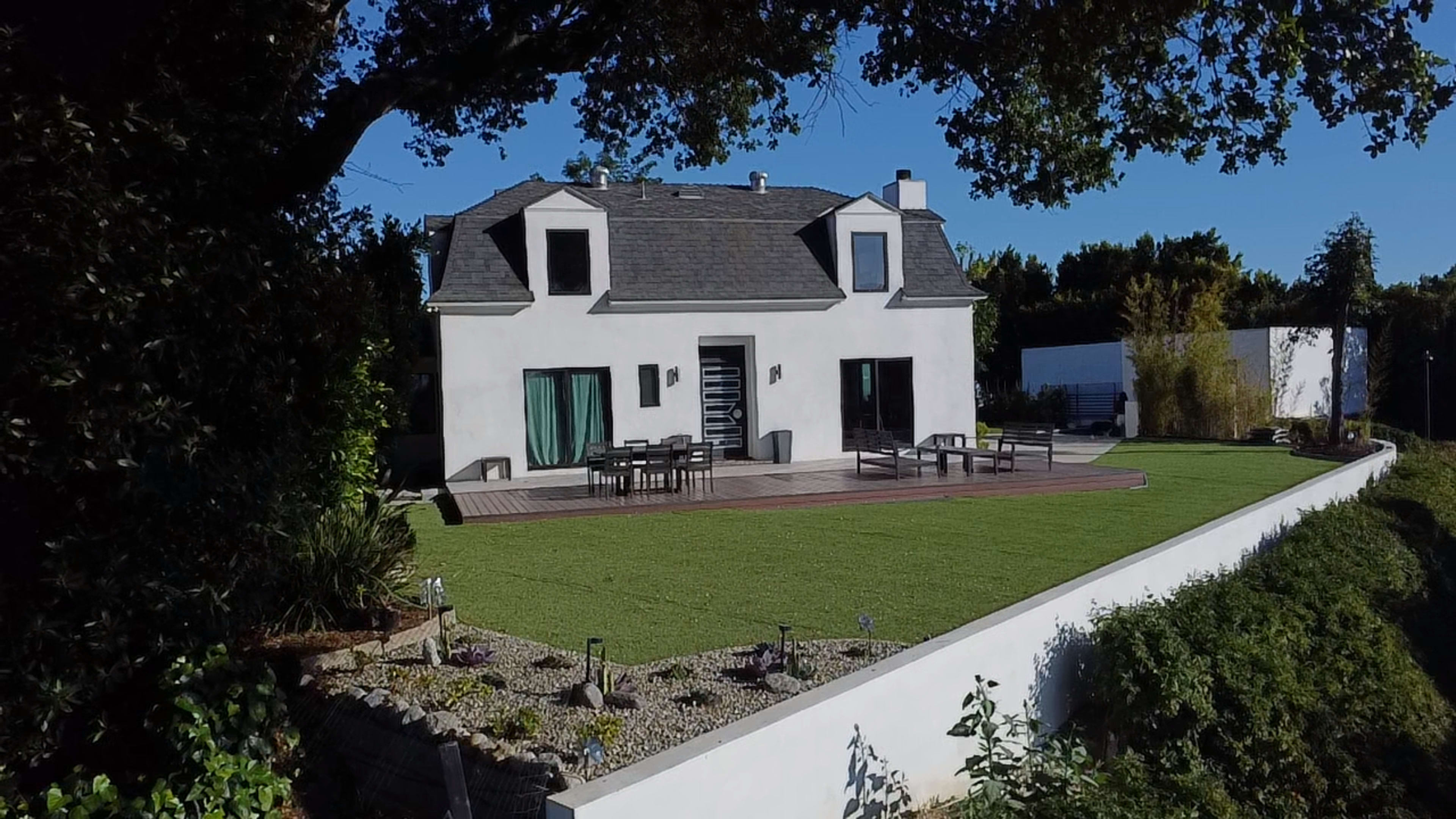 A modern two-story house with a sloped roof sits on a landscaped lawn surrounded by greenery.