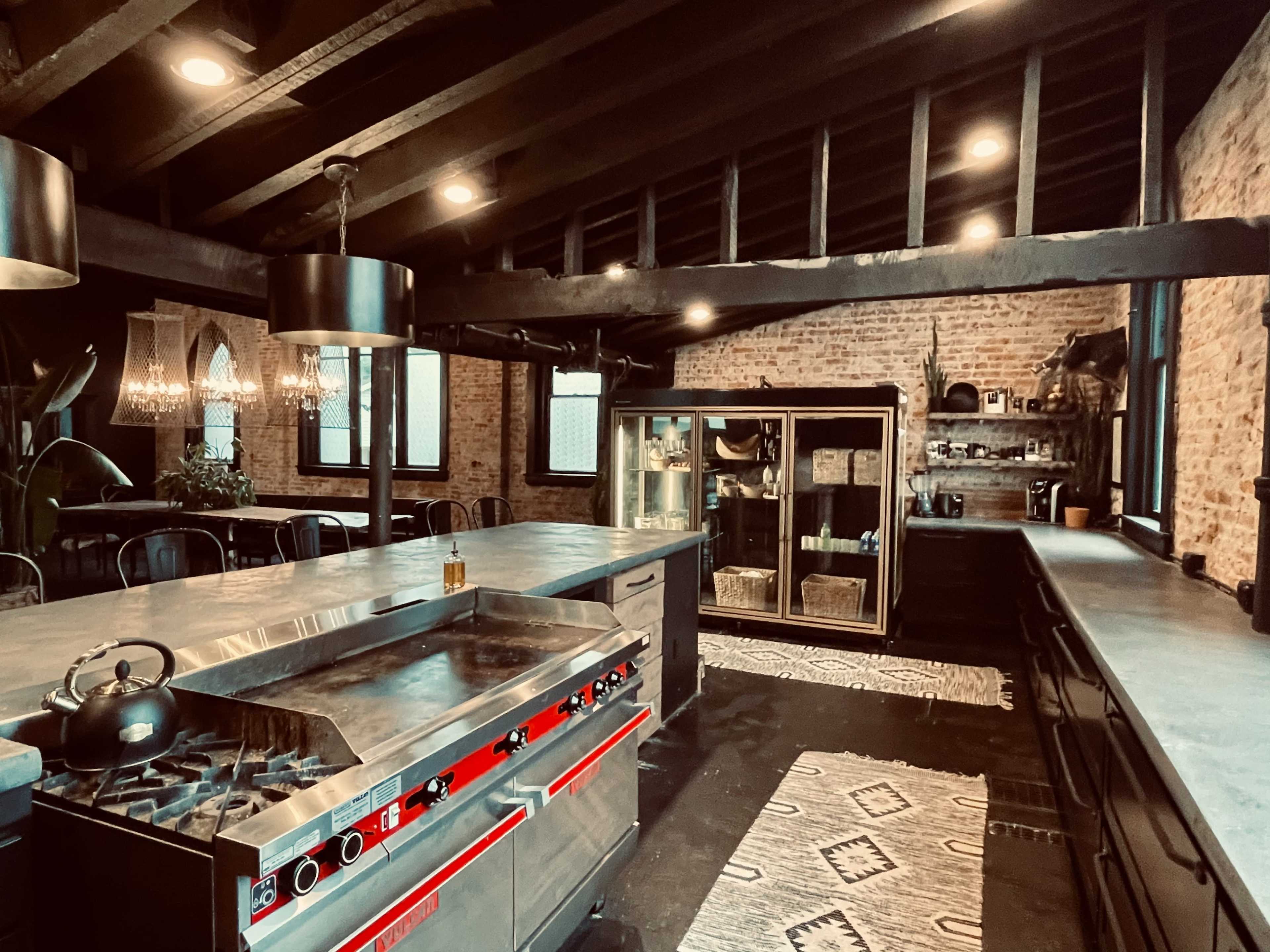 A modern kitchen with a large red gas stove, dark wooden beams, and industrial-style decor, featuring a mix of exposed brick walls and contemporary furnishings.