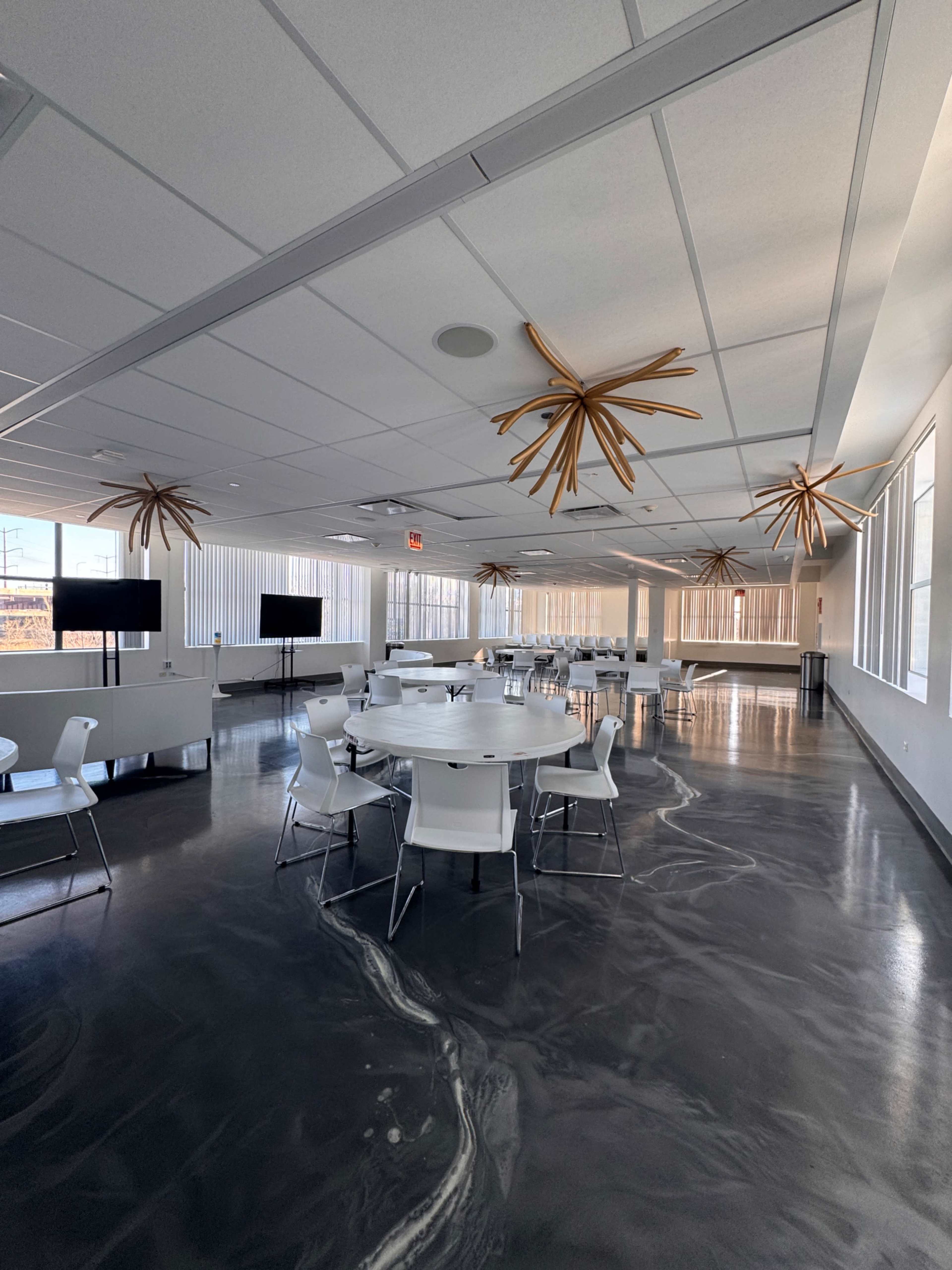 The image shows a modern meeting room with a polished floor, round tables, and unique wooden ceiling fixtures.