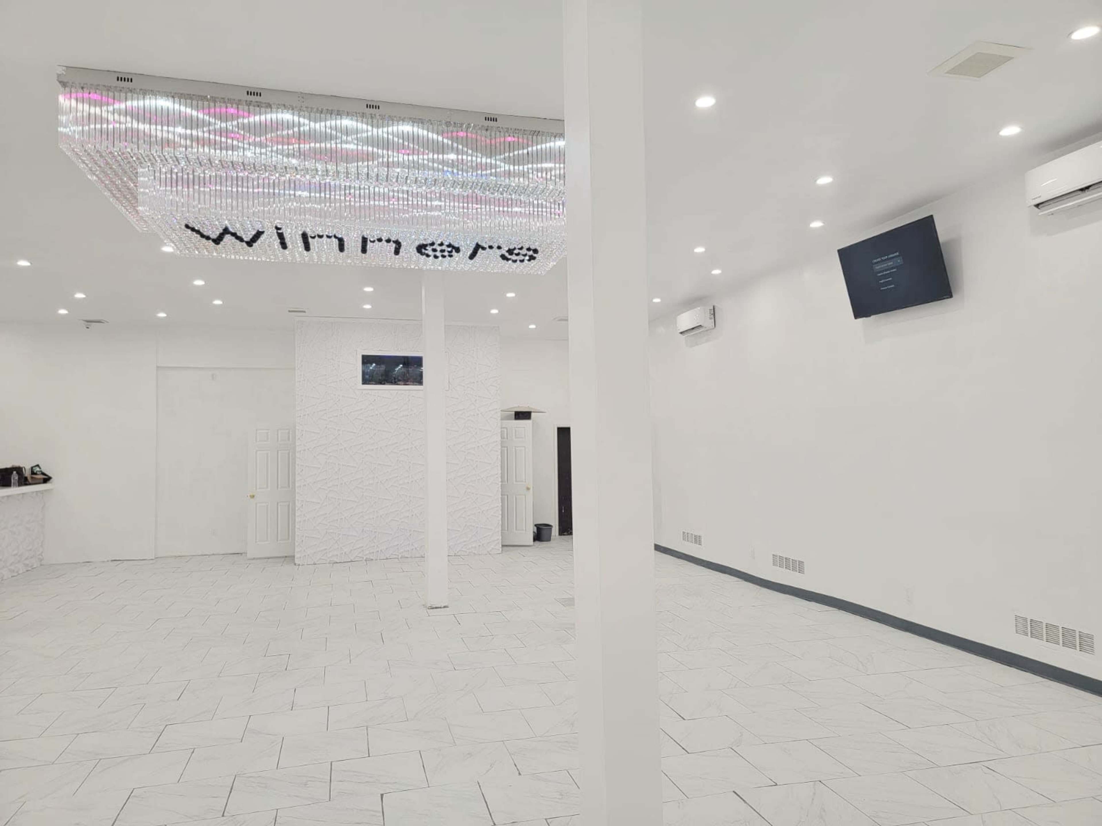 A spacious, white room with a chandelier labeled "winners" hanging from the ceiling and multiple air conditioning units on the walls.