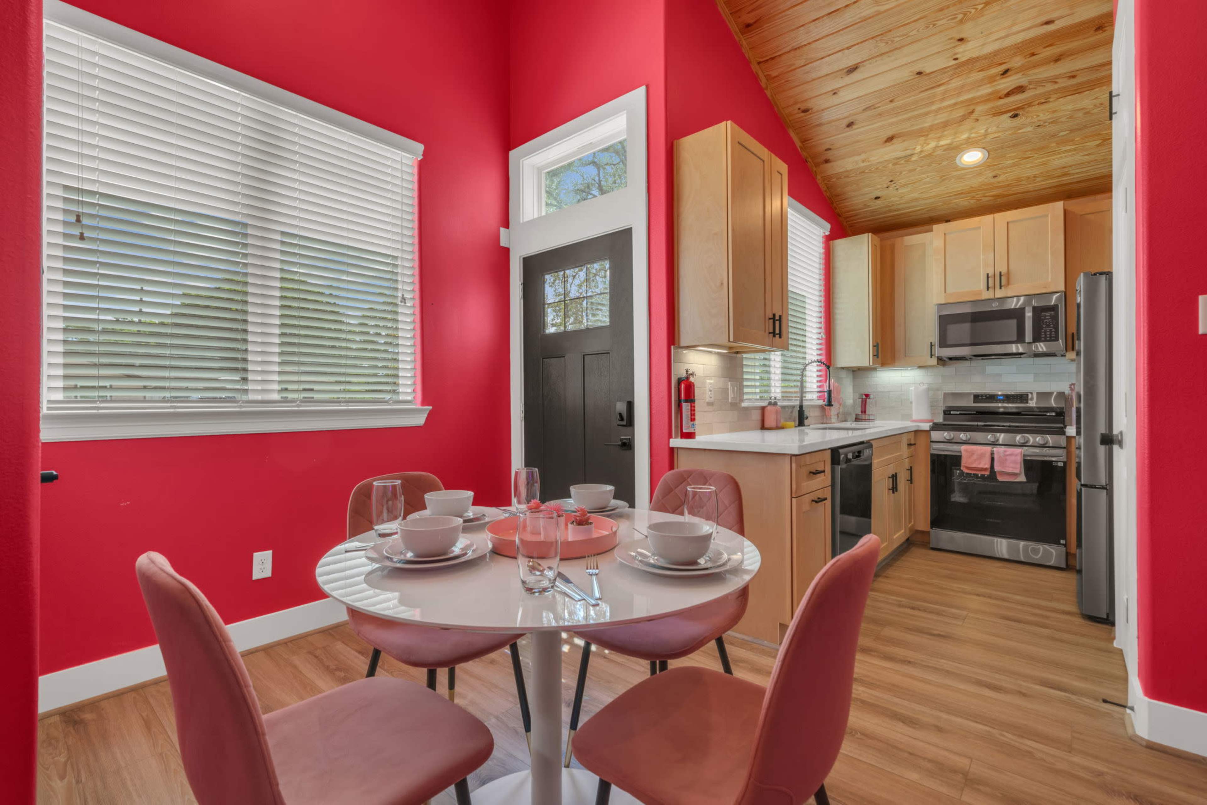 The image shows a modern kitchen and dining area with red walls, featuring a round table set for four and stainless steel appliances.