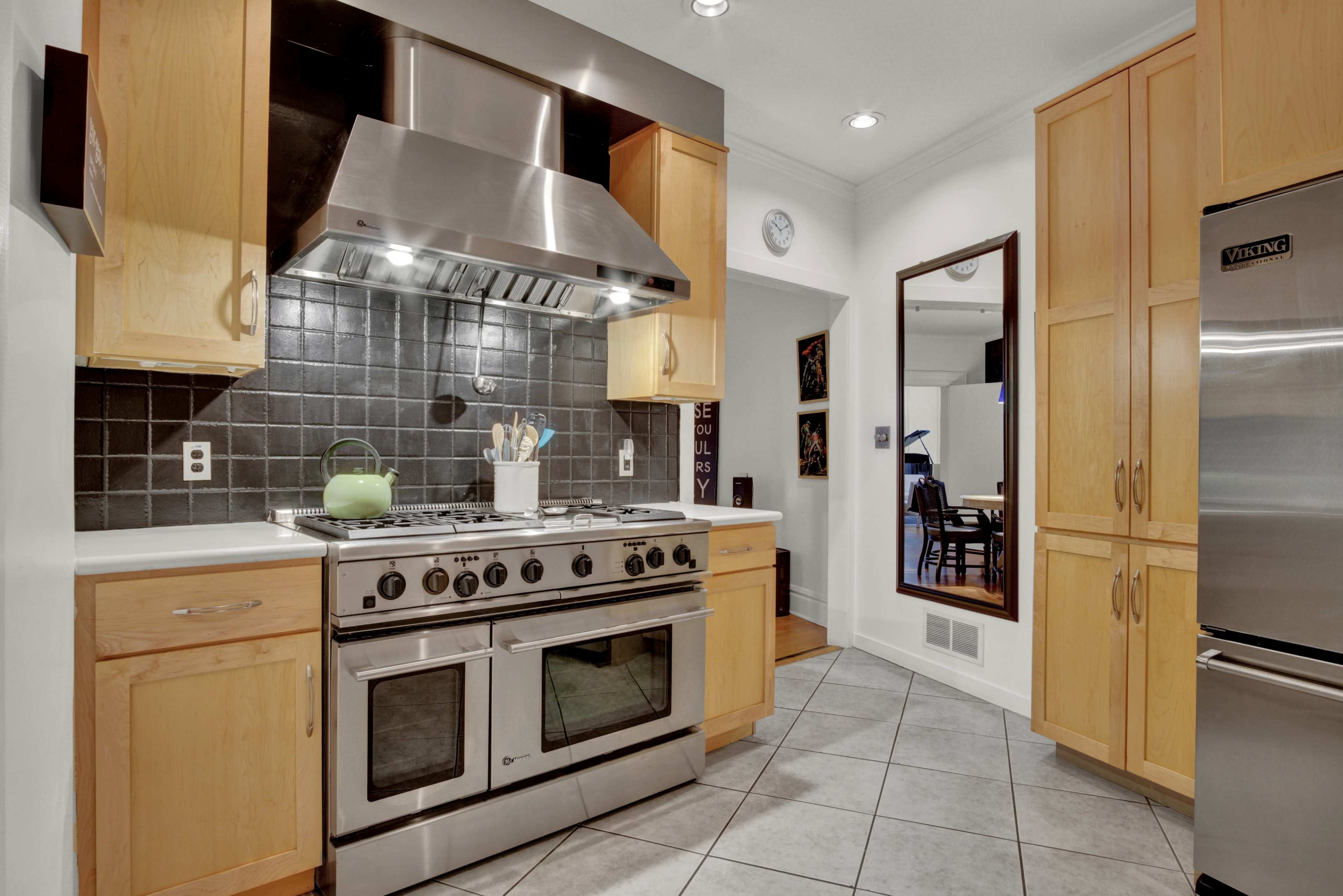 A modern kitchen with stainless steel appliances, wooden cabinets, and a tiled floor.