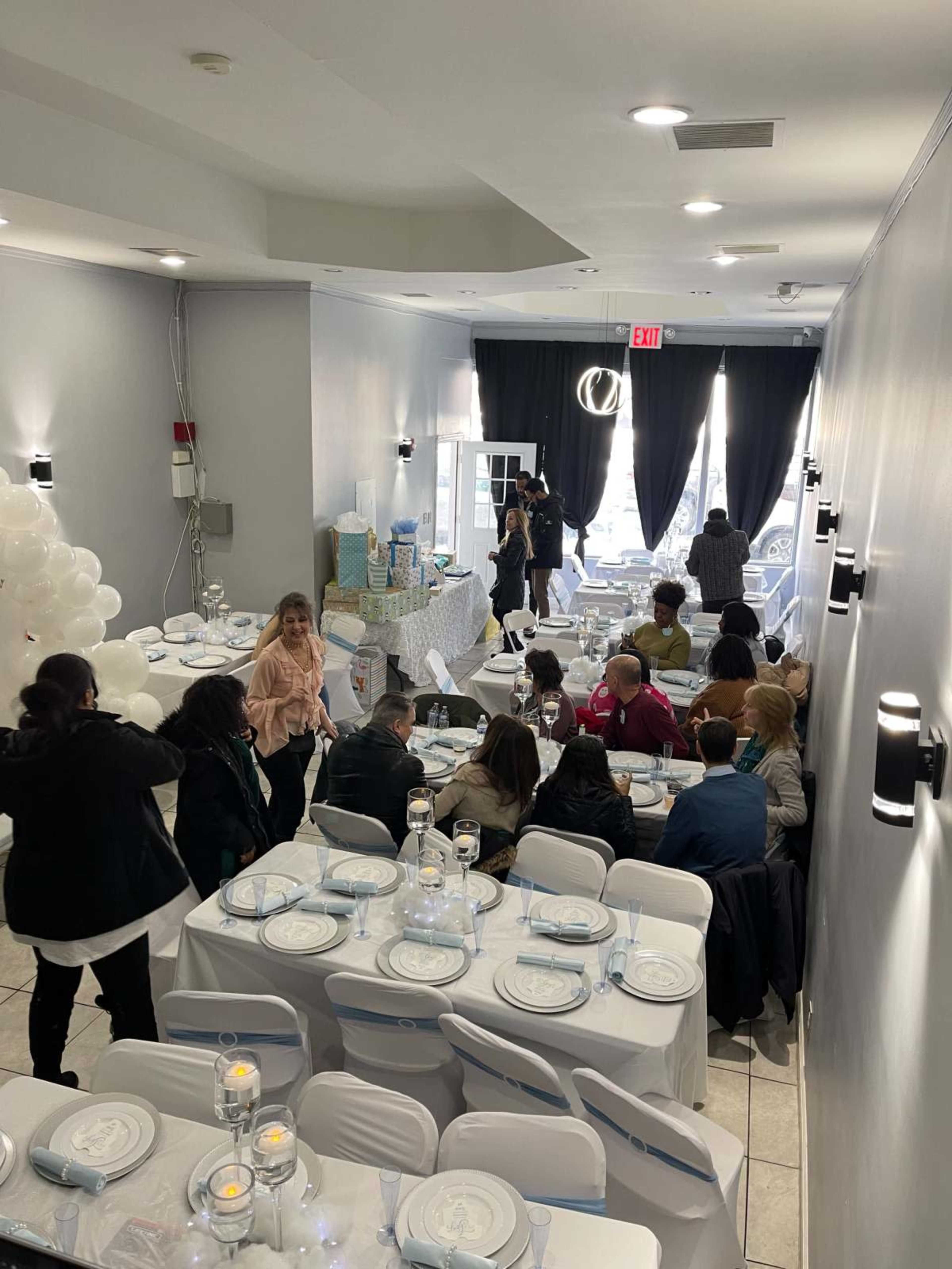 A group of people gathers around elegantly set tables in a well-decorated event space with white and blue decor.