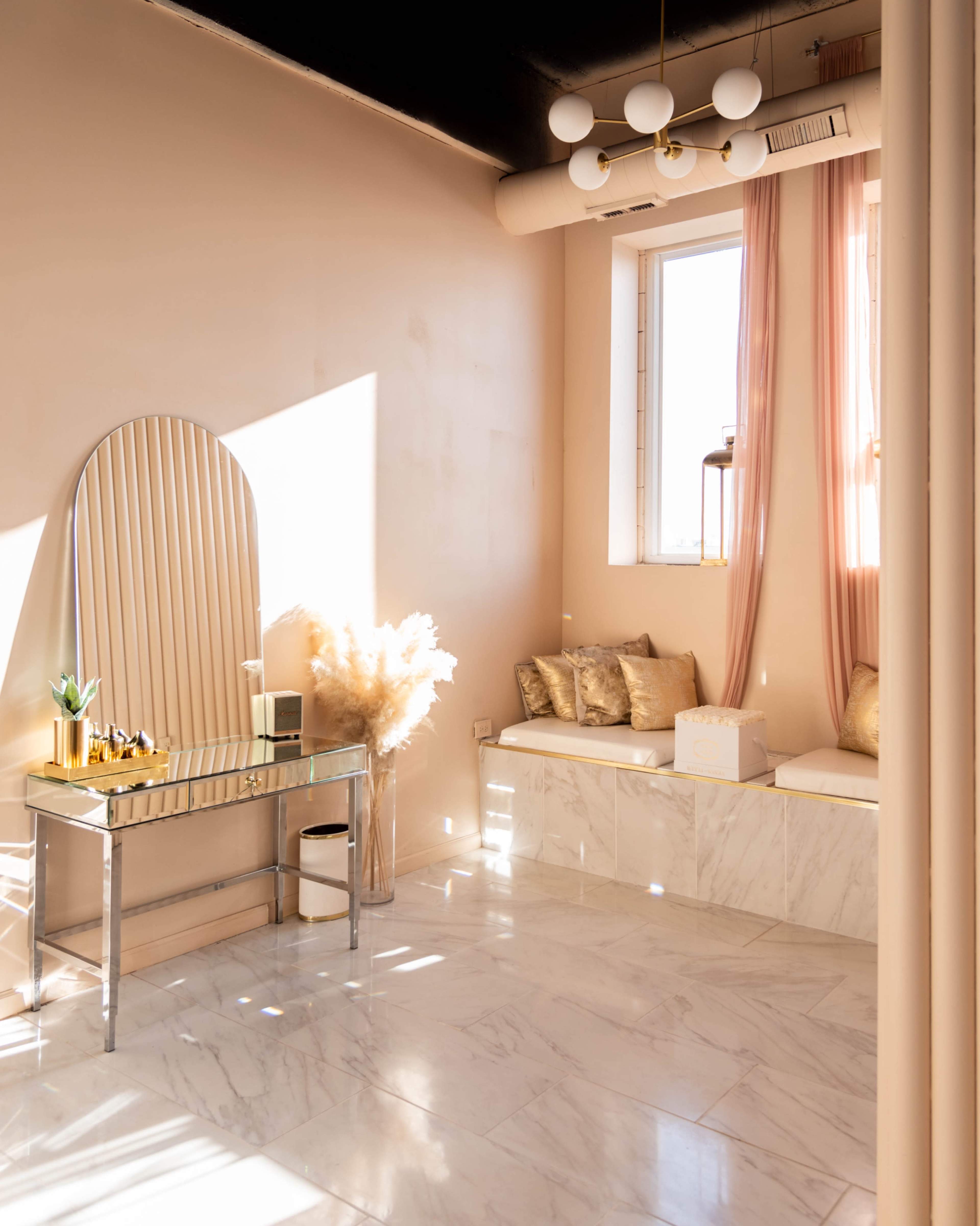 A minimalist interior space with a console table, plush seating, and decorative elements, illuminated by natural light streaming through a window.