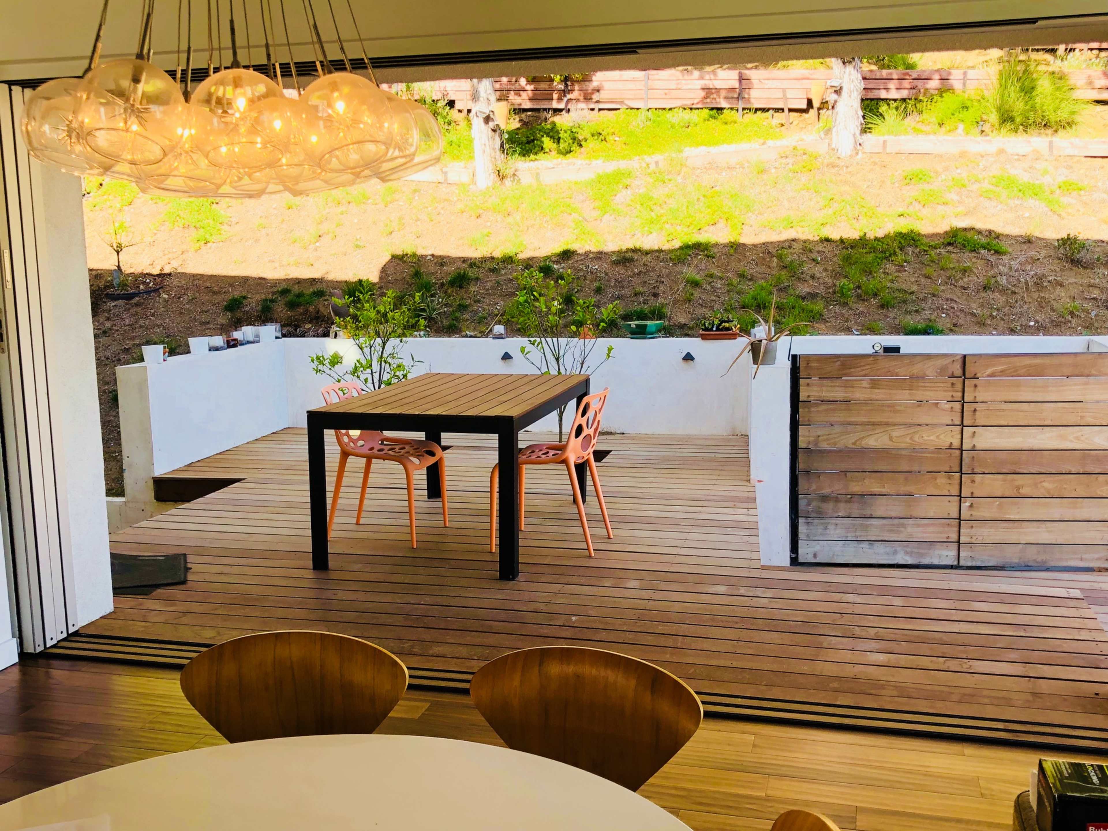 A wooden deck with a table and chairs overlooks a grassy area behind a house.