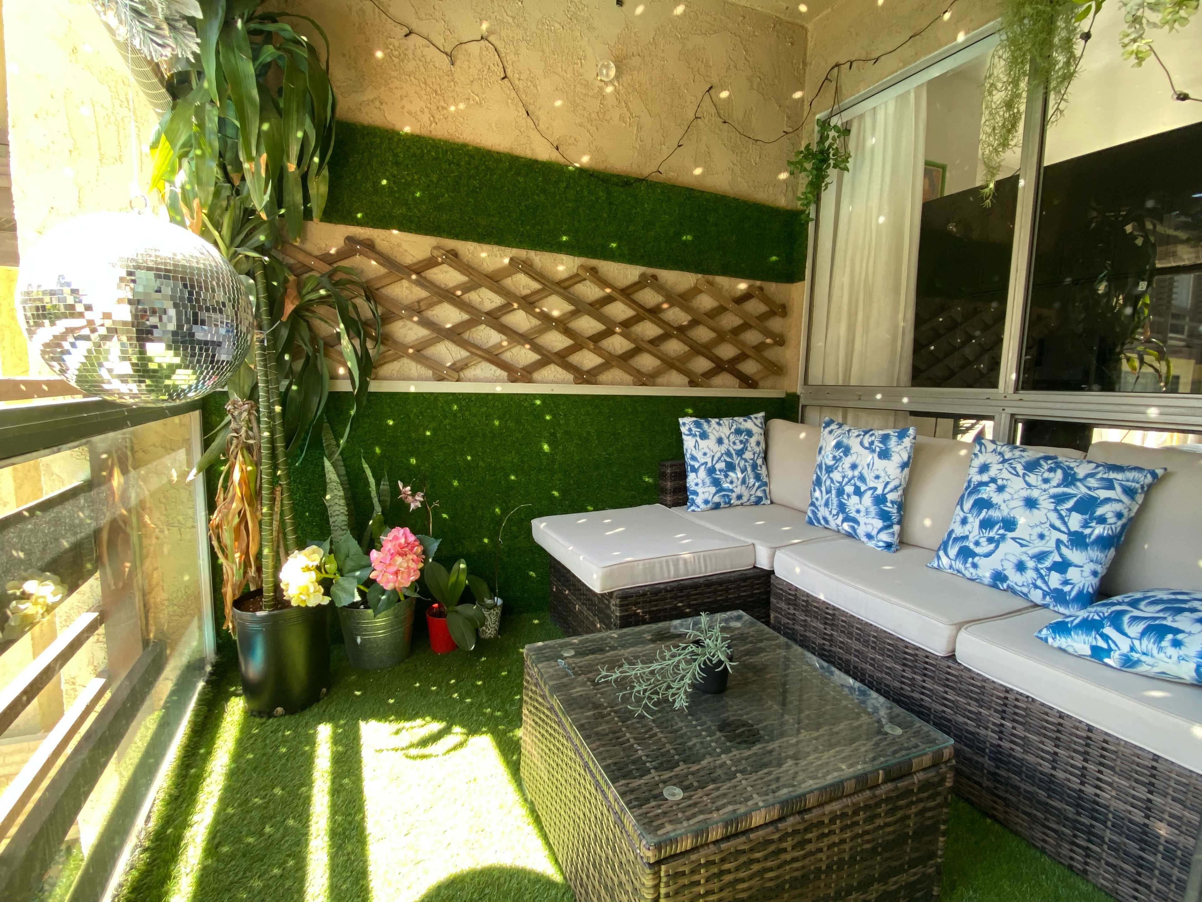 The image features a cozy patio with a wicker seating area, decorative pillows, potted plants, and a disco ball reflecting light.