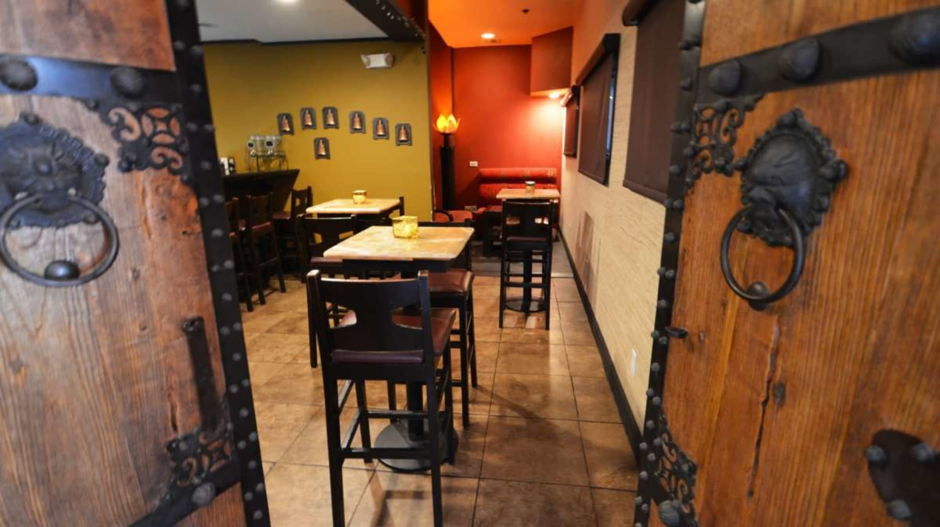 A restaurant interior with wooden double doors leading into a space featuring tables, chairs, and framed pictures on the walls.