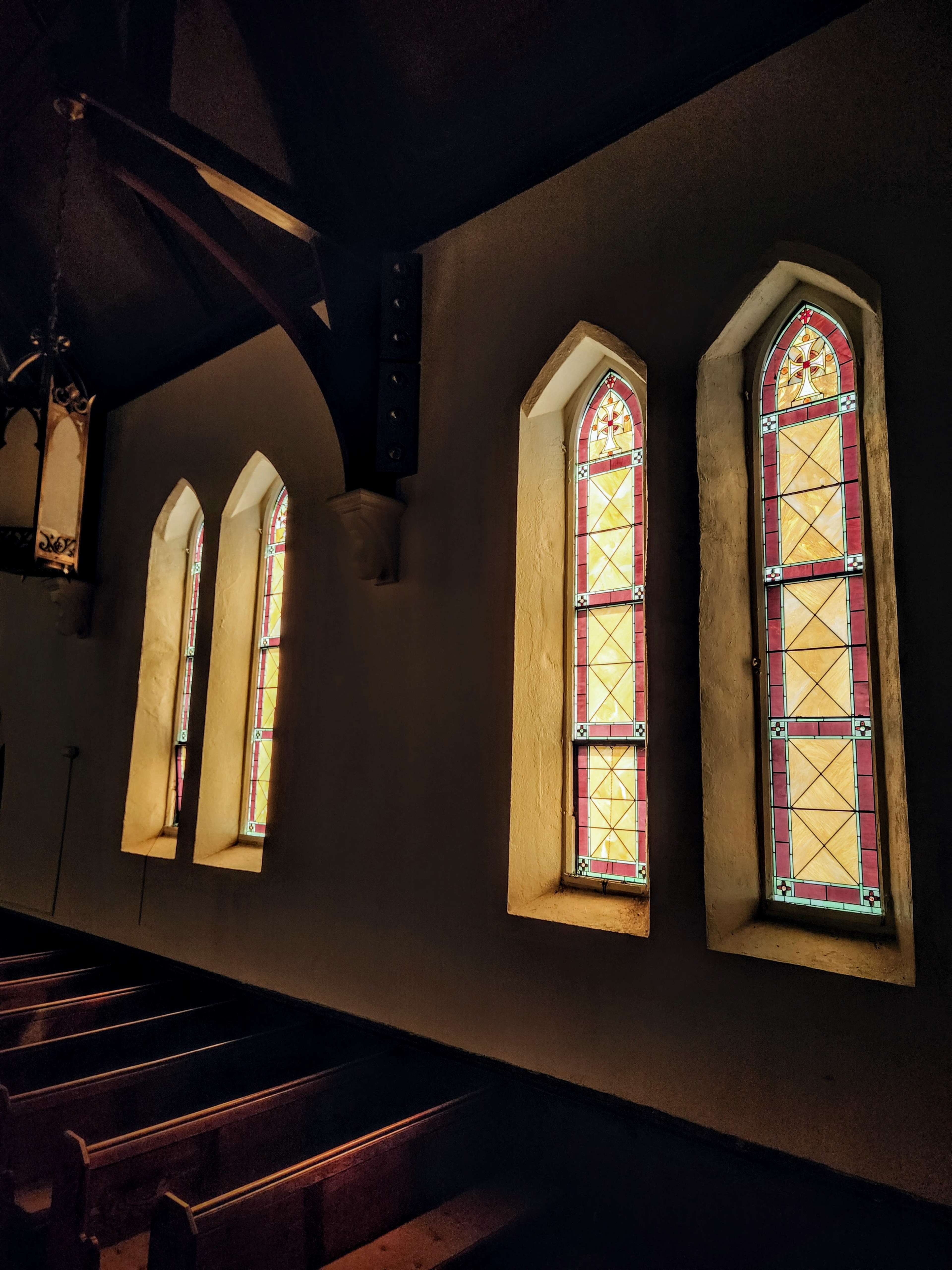 Three tall, narrow stained glass windows illuminated by soft light in a church interior.