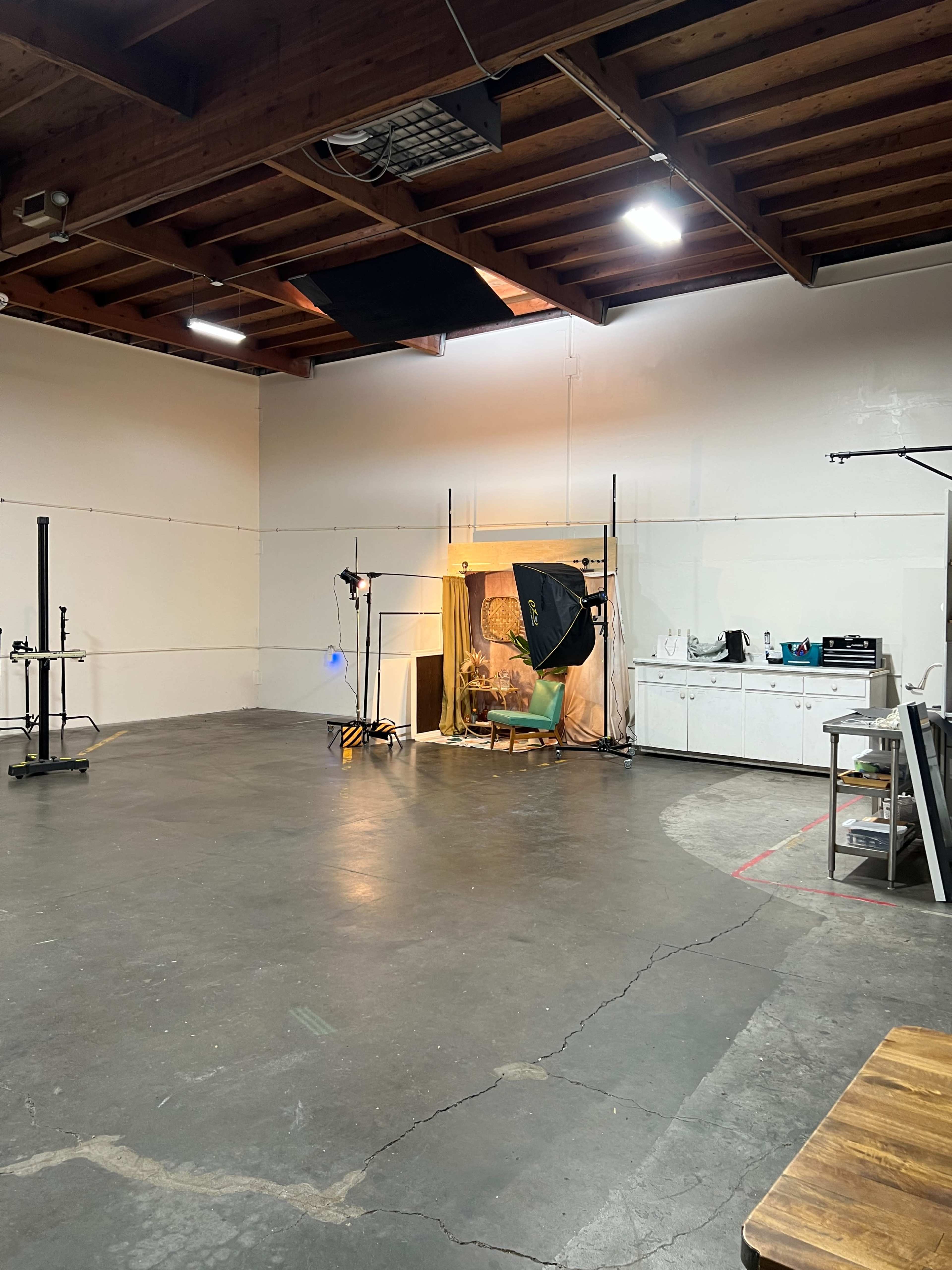 The image shows an empty studio space with a backdrop setup, lighting equipment, and various tools against the walls.