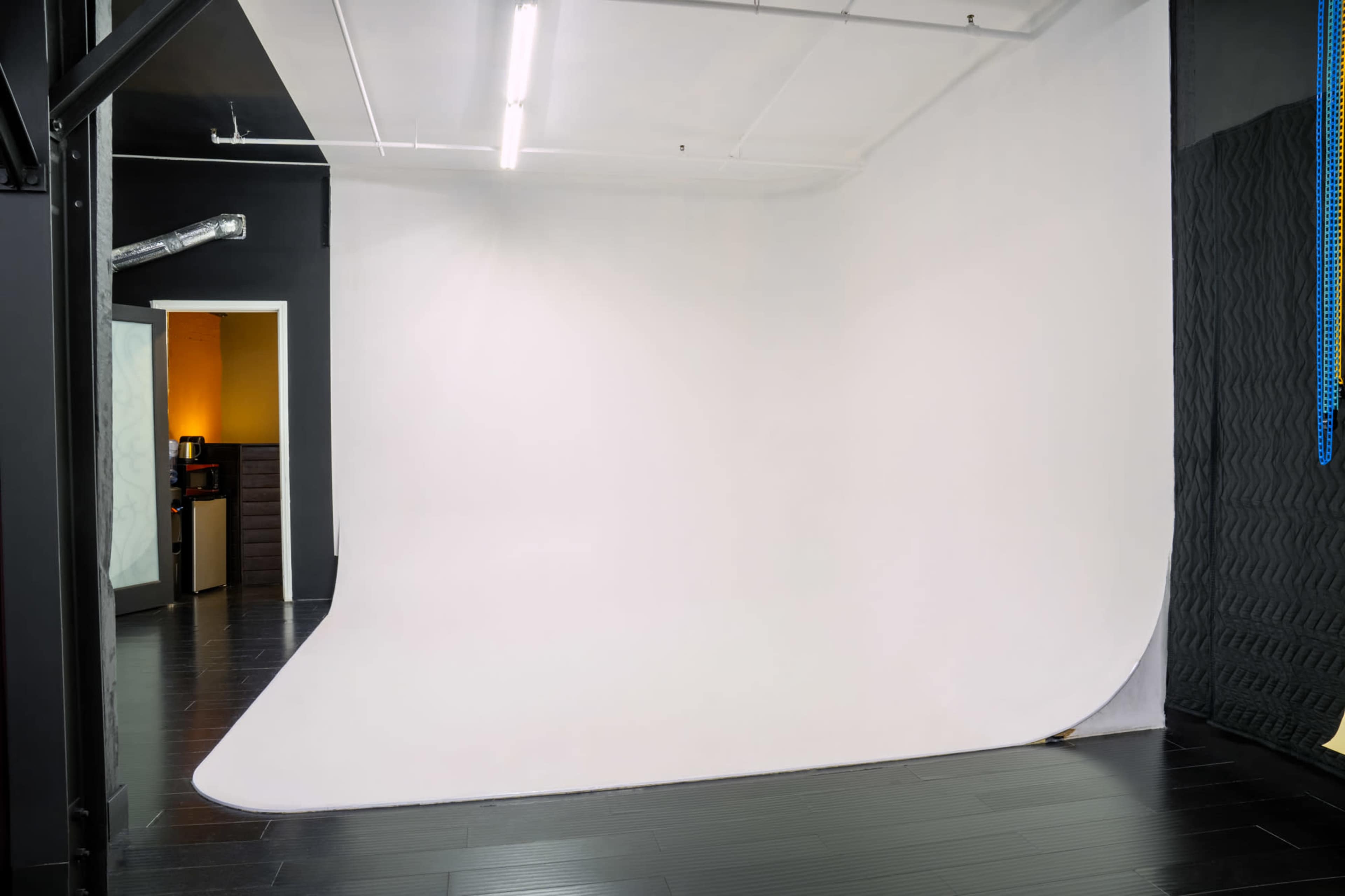 The image shows a photography studio with a seamless white backdrop, black flooring, and minimal furnishings in the background.