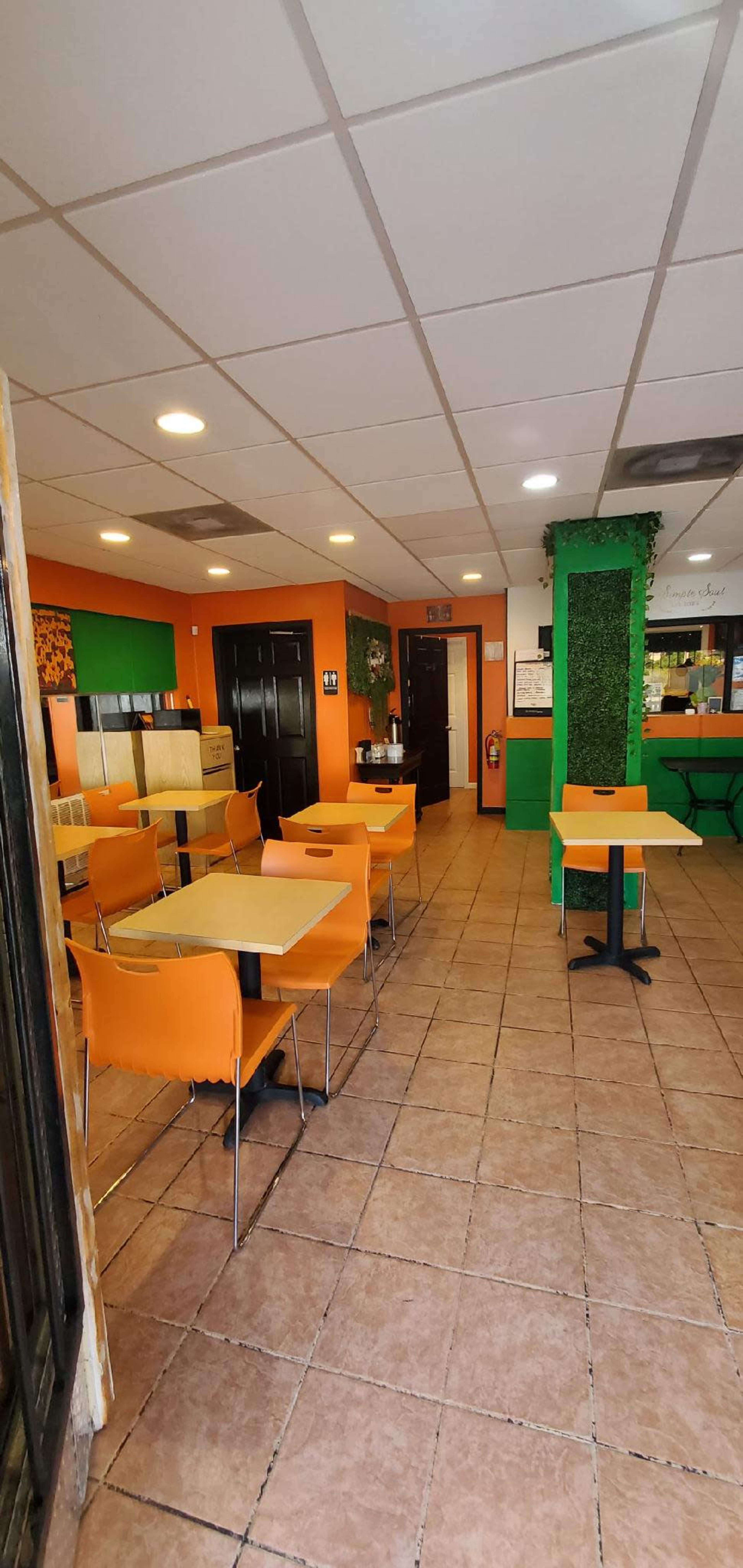 A spacious restaurant interior with orange and green walls, featuring several empty tables and chairs arranged throughout the area.