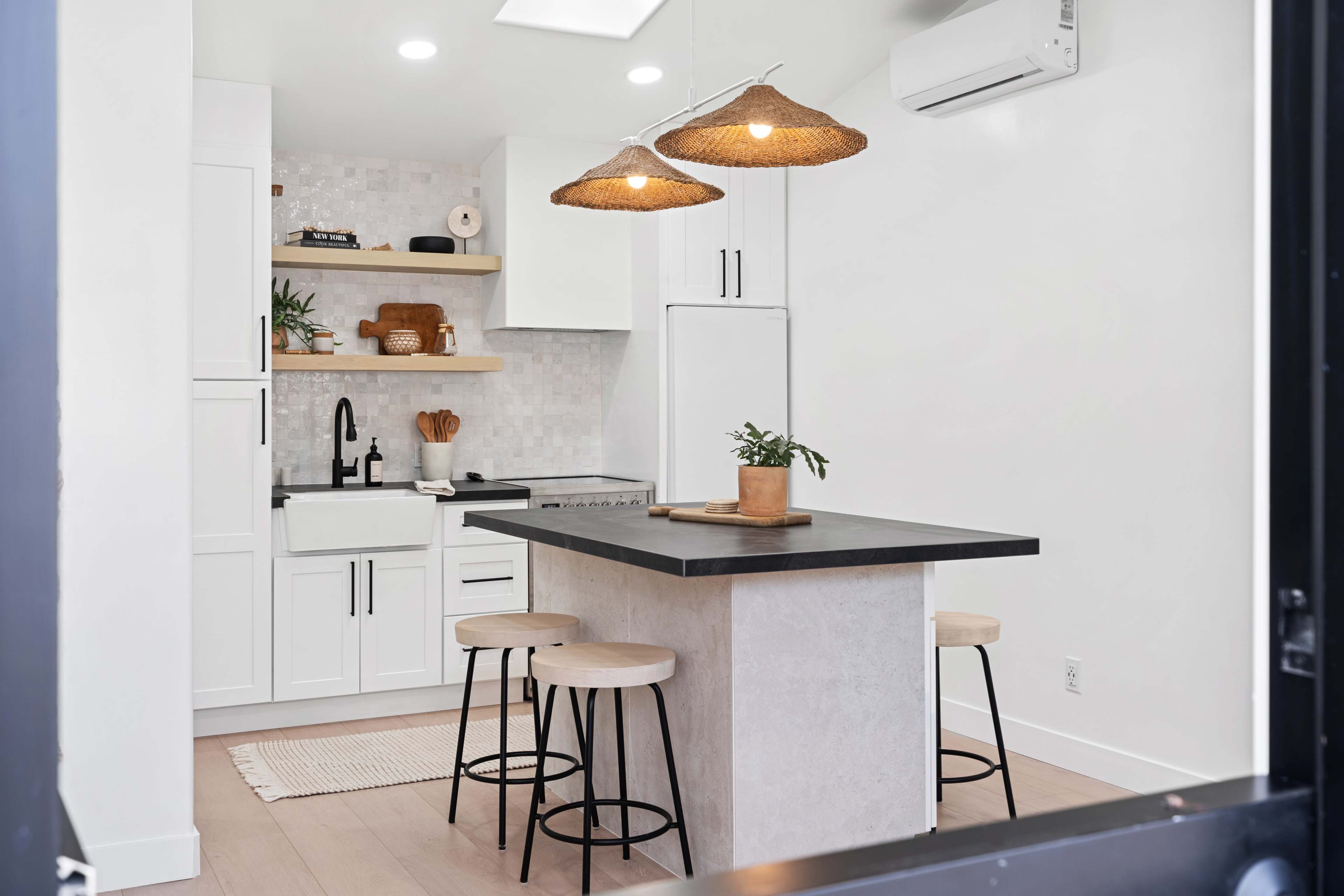 A modern kitchen features a central island with three stools, pendant lights, and white cabinetry against a light-colored backsplash.