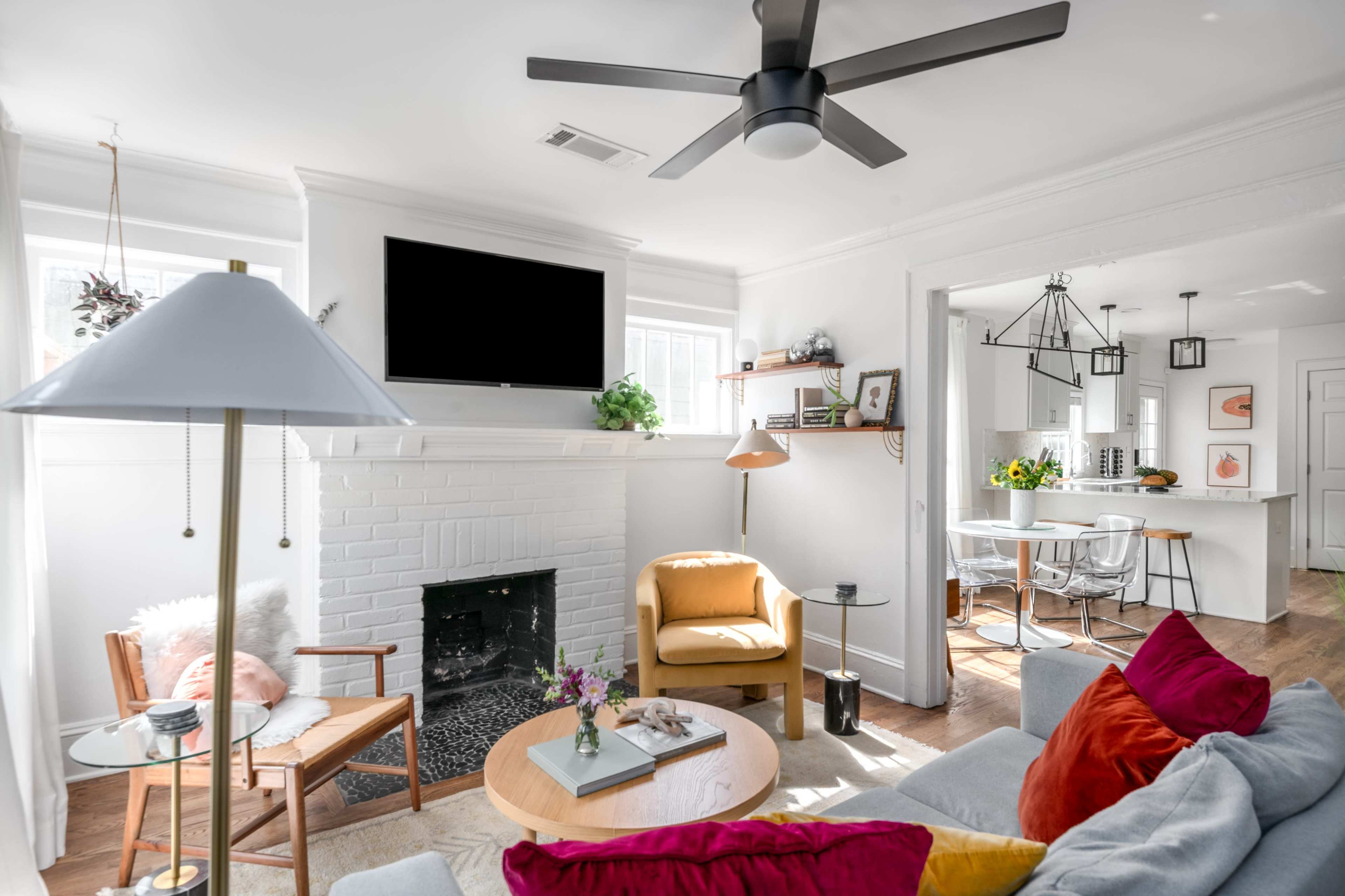 The living room features a white-brick fireplace, a ceiling fan, and modern furniture arranged to create a cozy atmosphere.