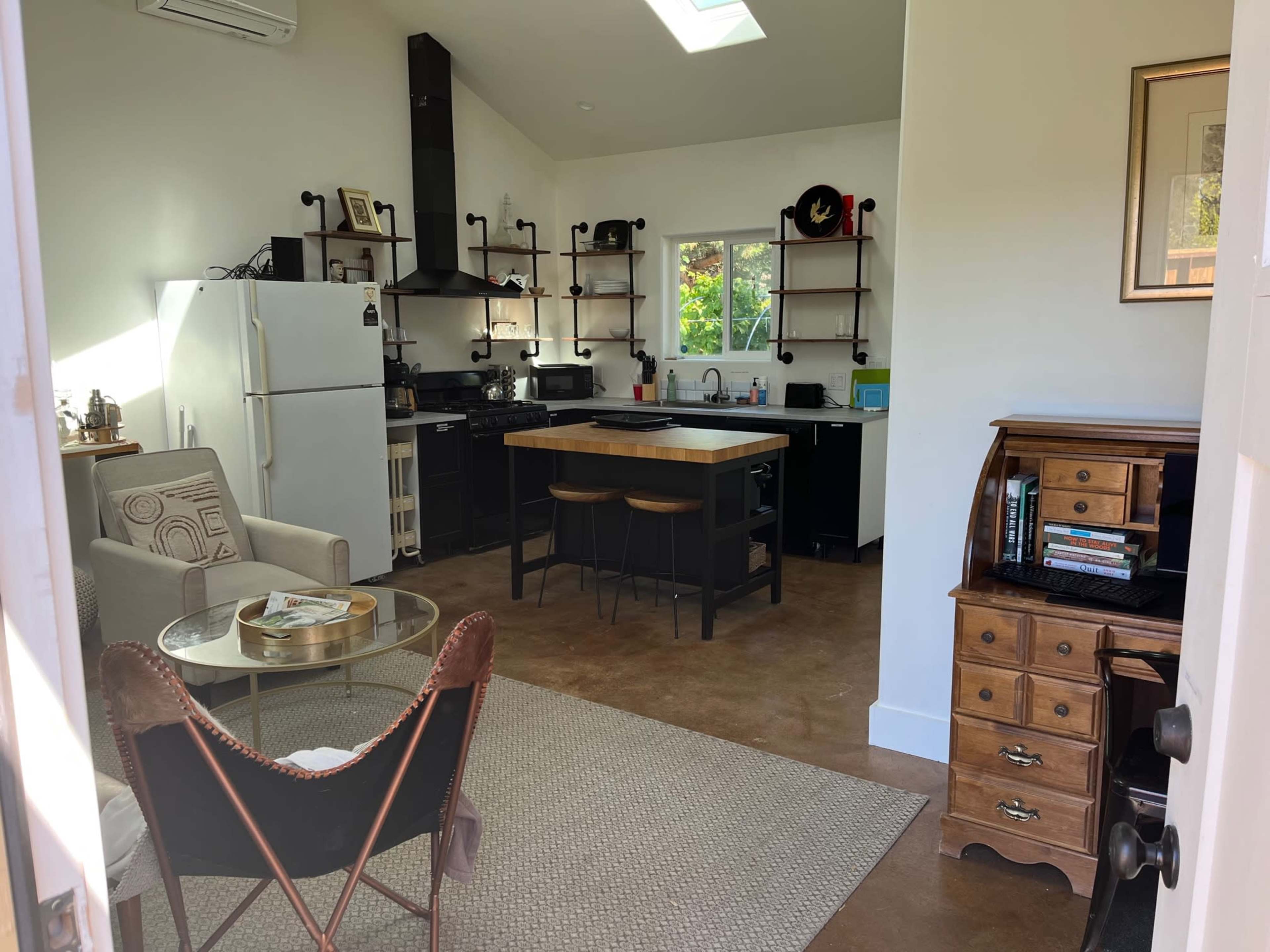 An open-concept kitchen and living area featuring a white refrigerator, black cabinetry, a wooden island with seating, and a combination of modern and vintage furnishings.