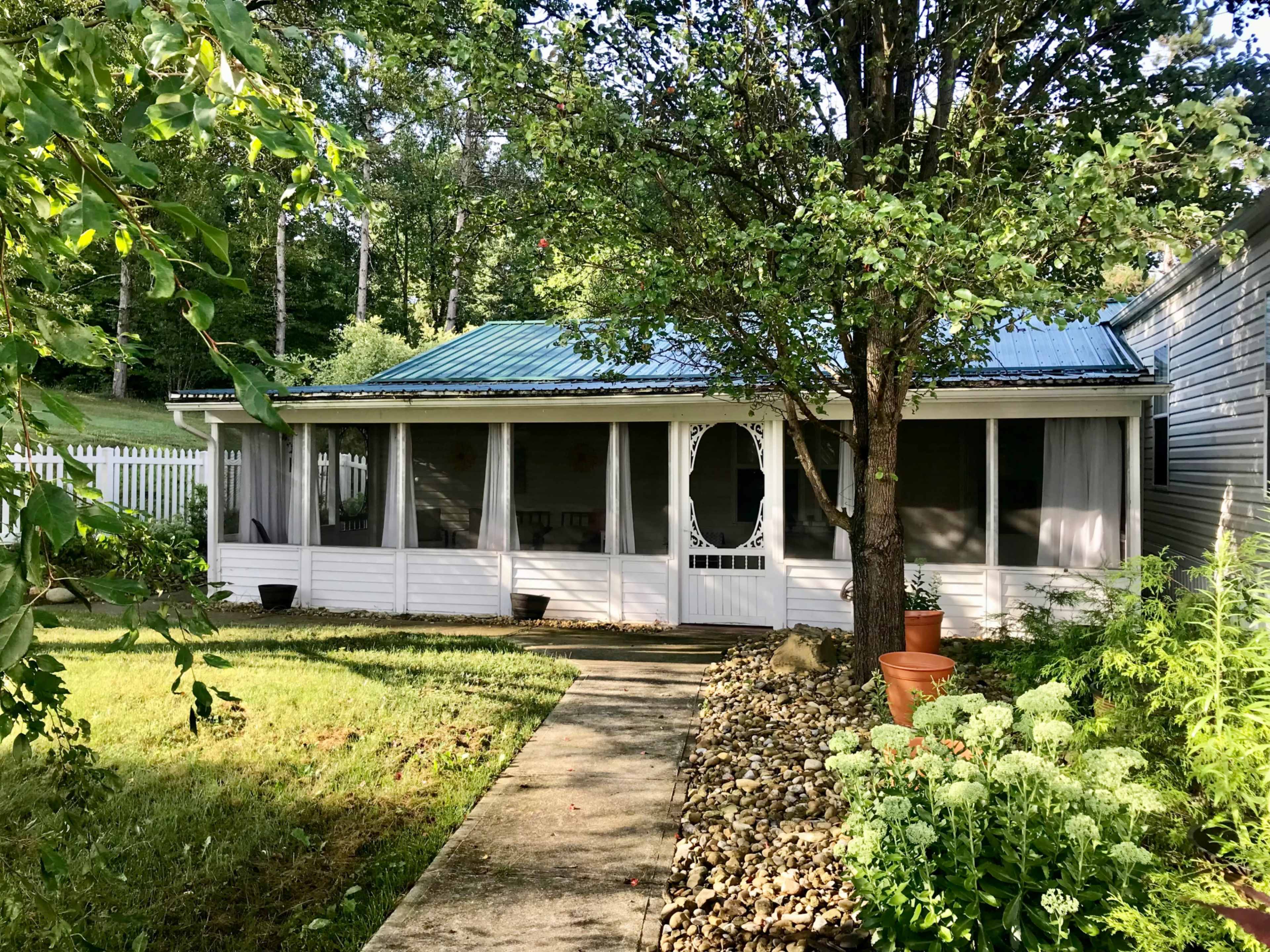 A house with a covered porch, surrounded by greenery, features a stone pathway leading to the entrance.
