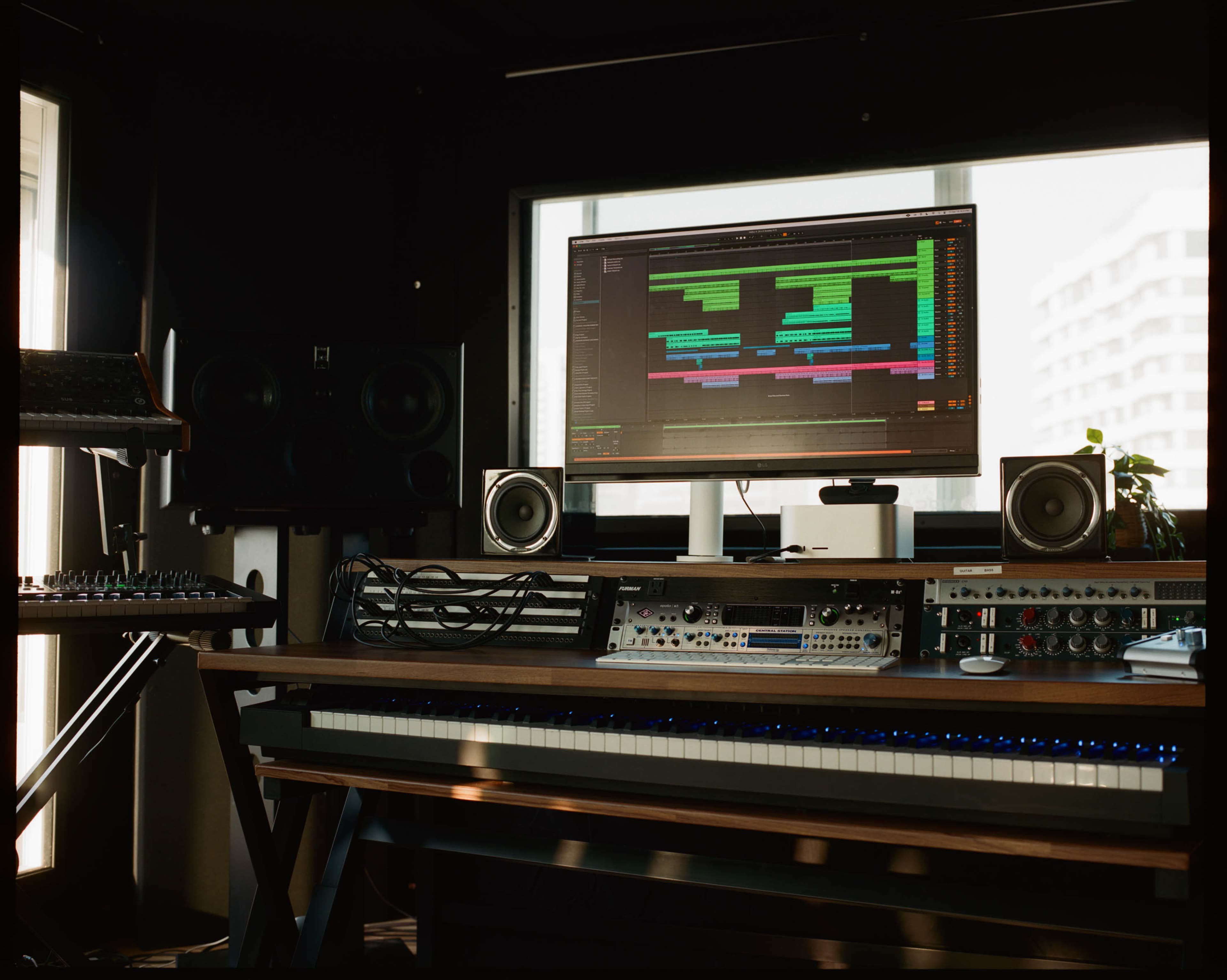 The image shows a modern music studio featuring a keyboard, audio equipment, and a large computer monitor displaying a music production software interface.