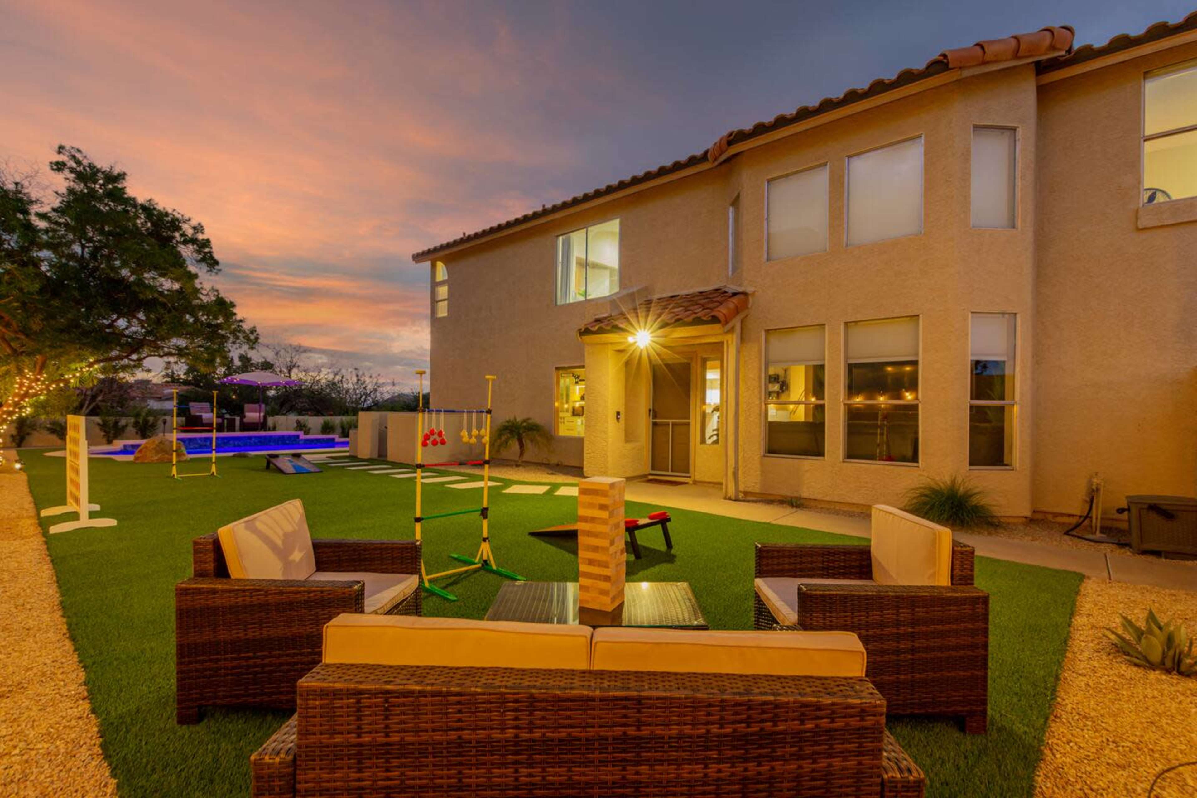 A well-appointed backyard features a seating area with wicker furniture, a grassy lawn, and a backdrop of a two-story house at sunset.