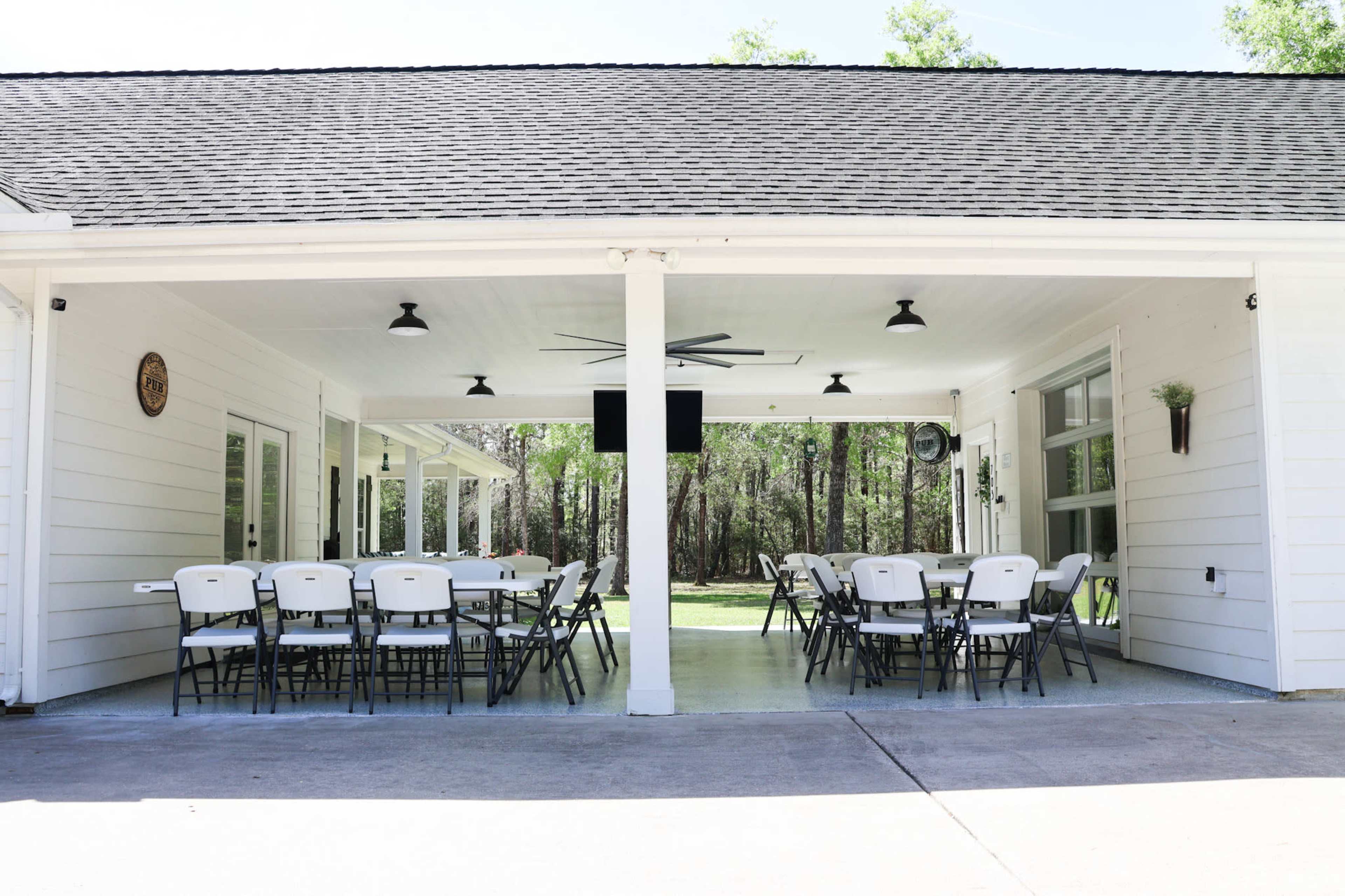 An outdoor pavilion features several folding chairs arranged around tables, with a grassy area visible in the background.