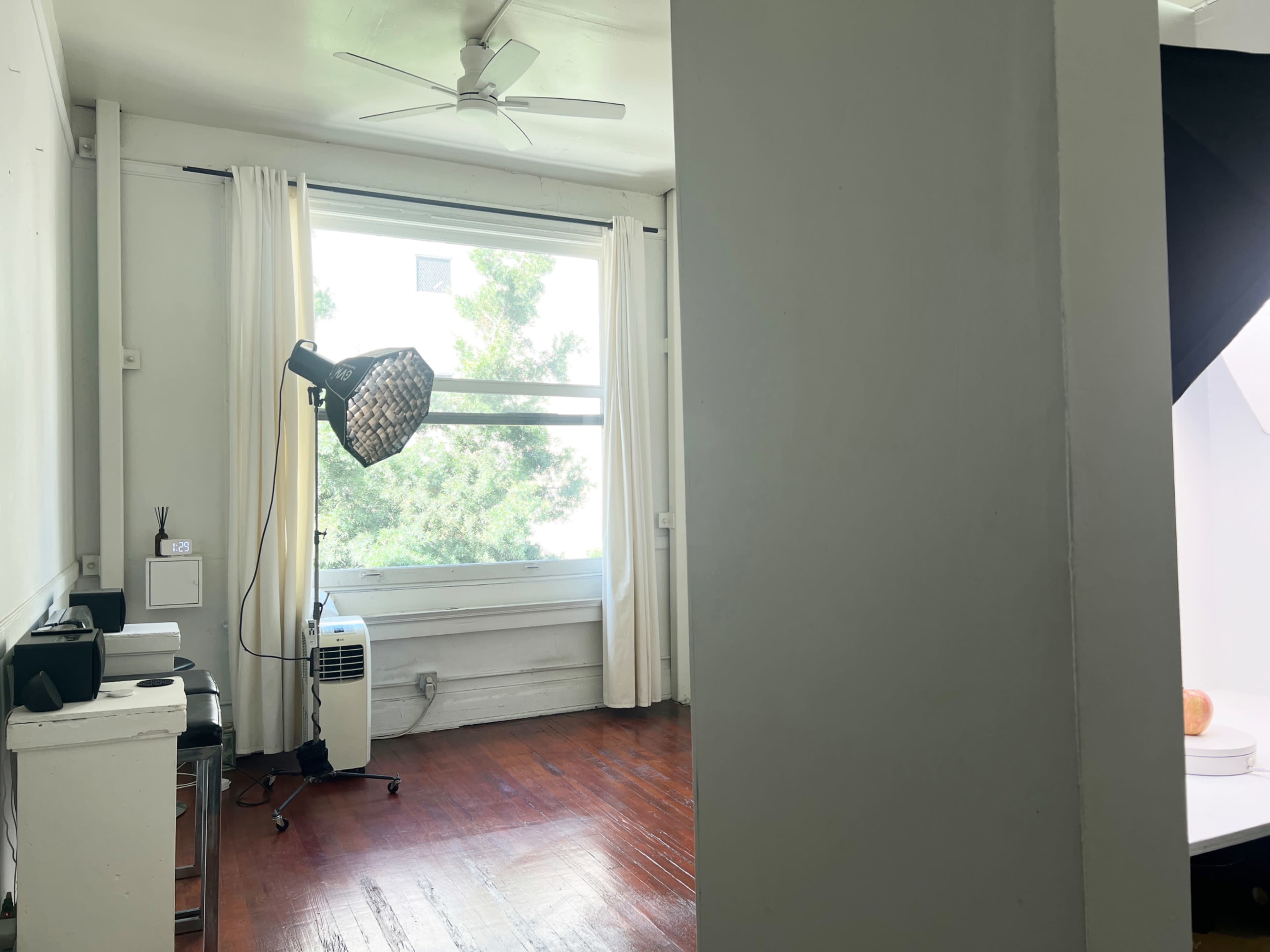 The image shows a bright room with large curtains and a standing light source, along with a visible window and wooden flooring.