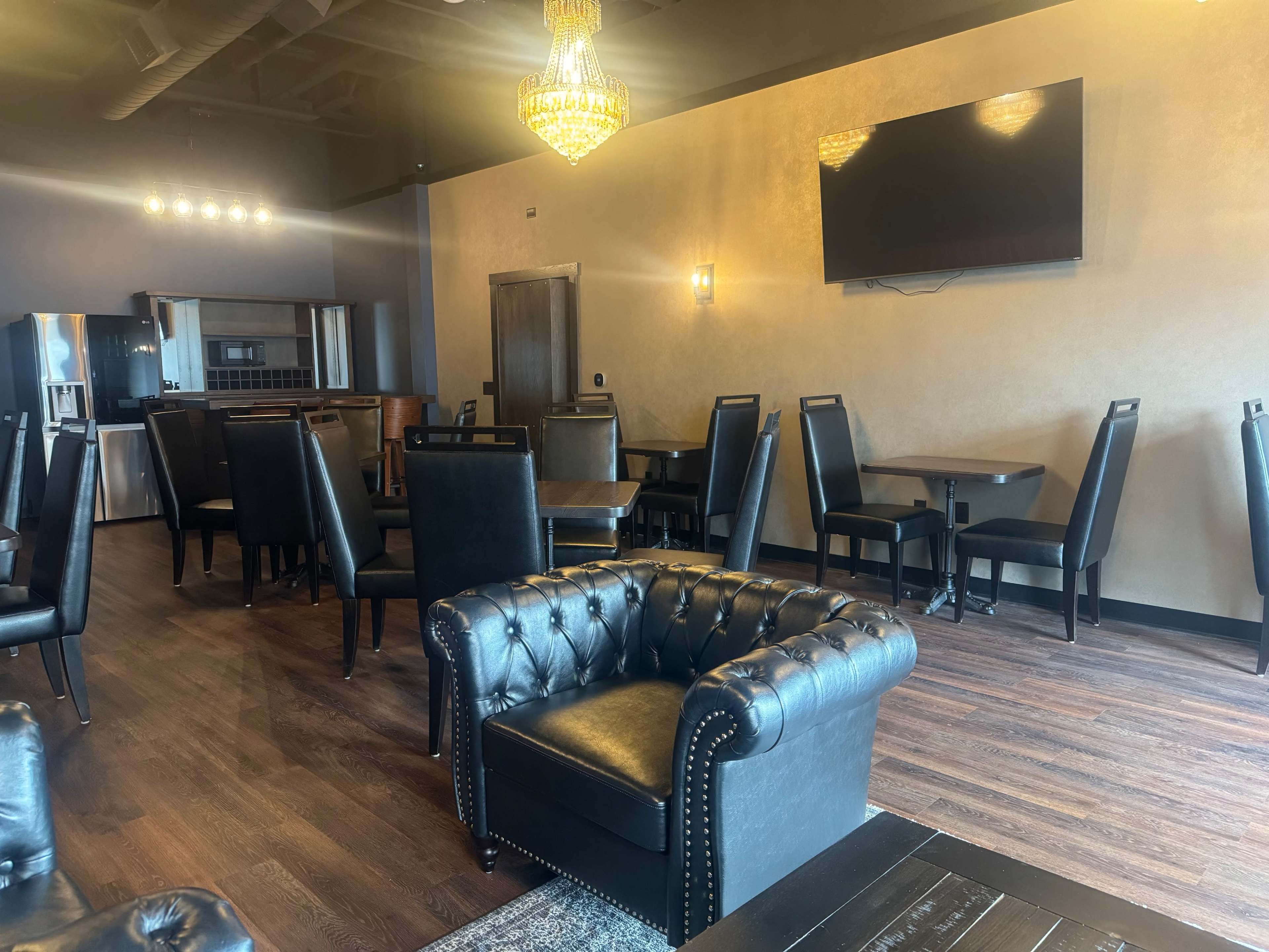 The image shows a modern dining area with black upholstered chairs, wooden tables, and a large chandelier hanging from the ceiling.