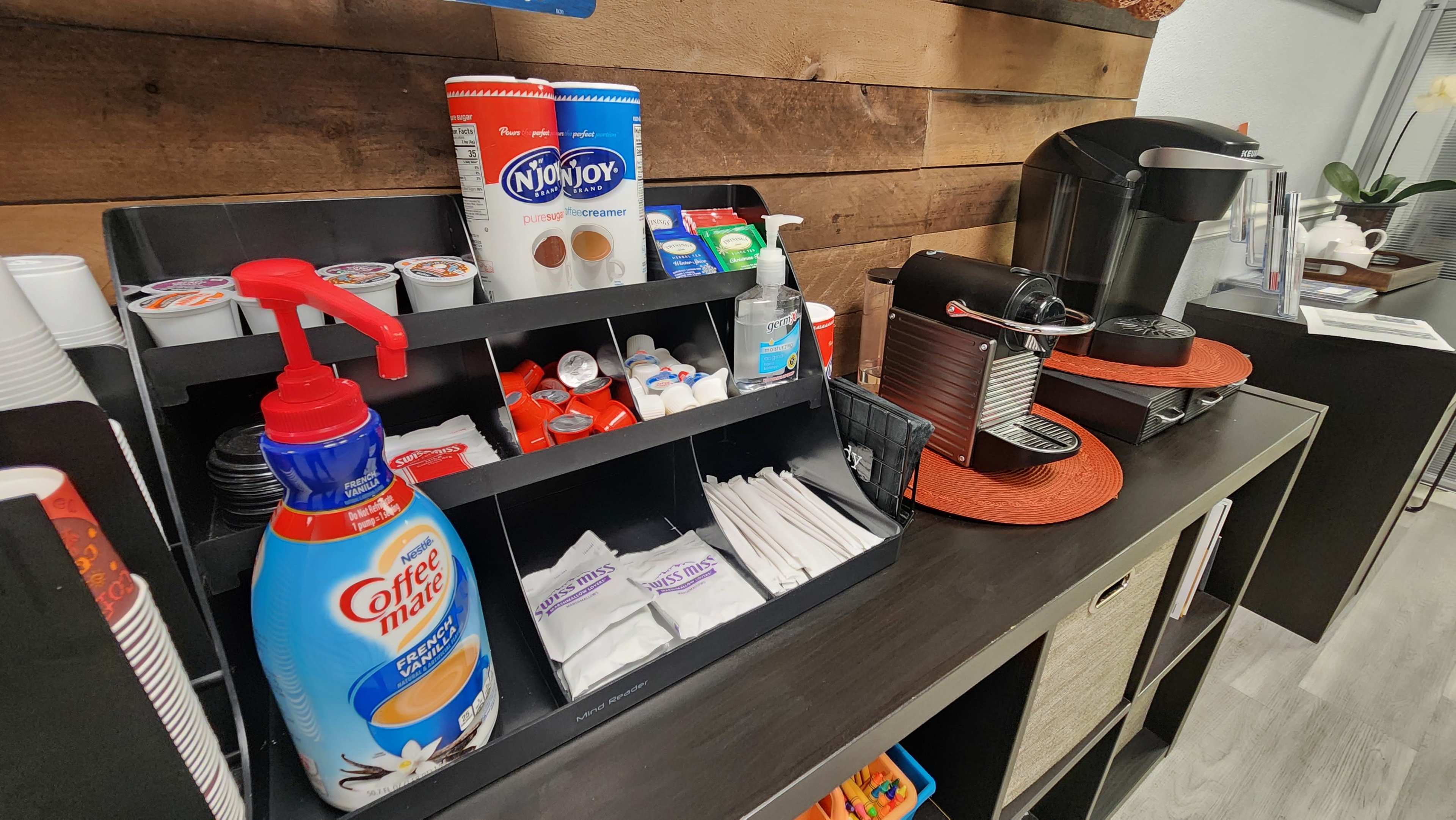 A countertop features a coffee station with condiments, including creamers, sugar packets, and a coffee maker.