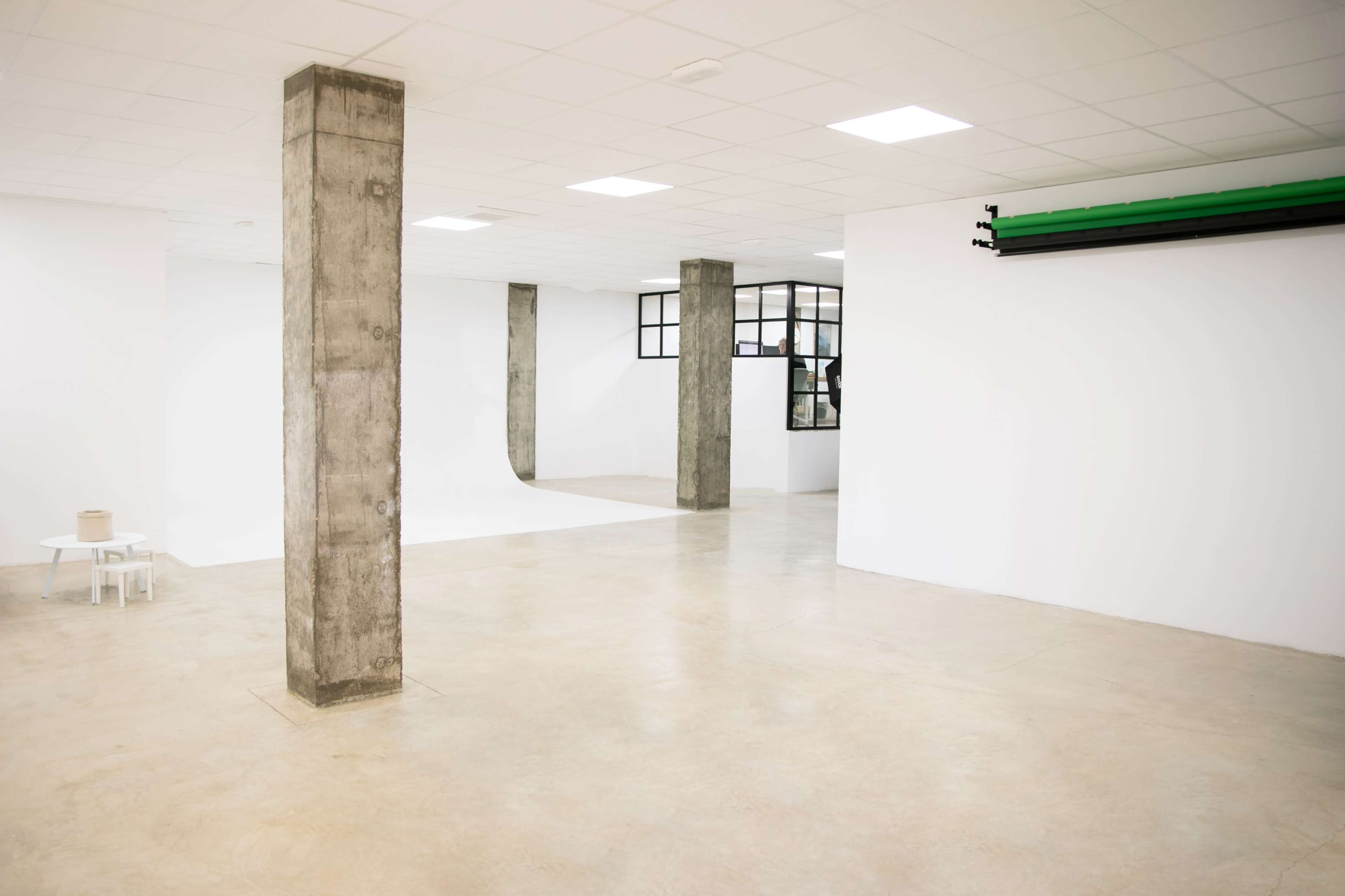The image shows an empty studio space with concrete pillars, white walls, and a light-colored floor.