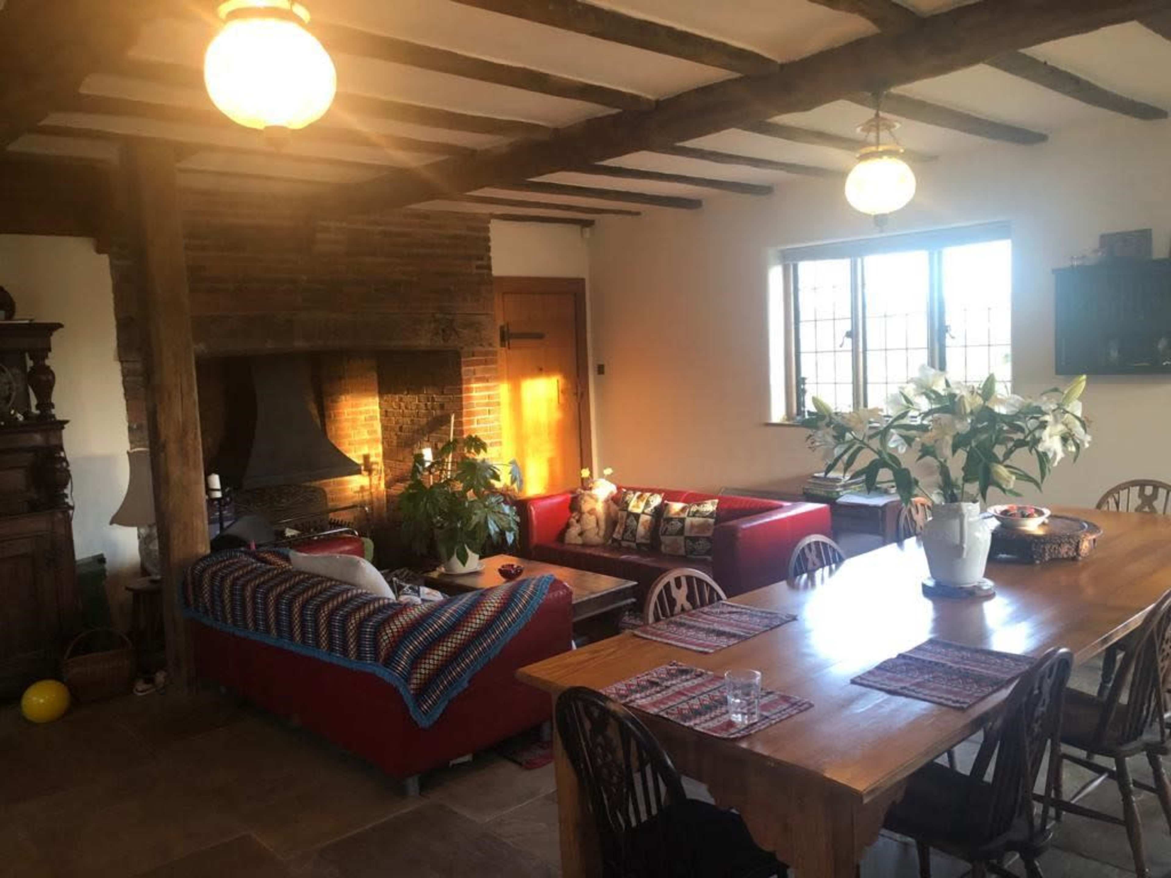 A spacious living area with a red couch, a wooden dining table, and a stone fireplace, illuminated by two hanging lights.