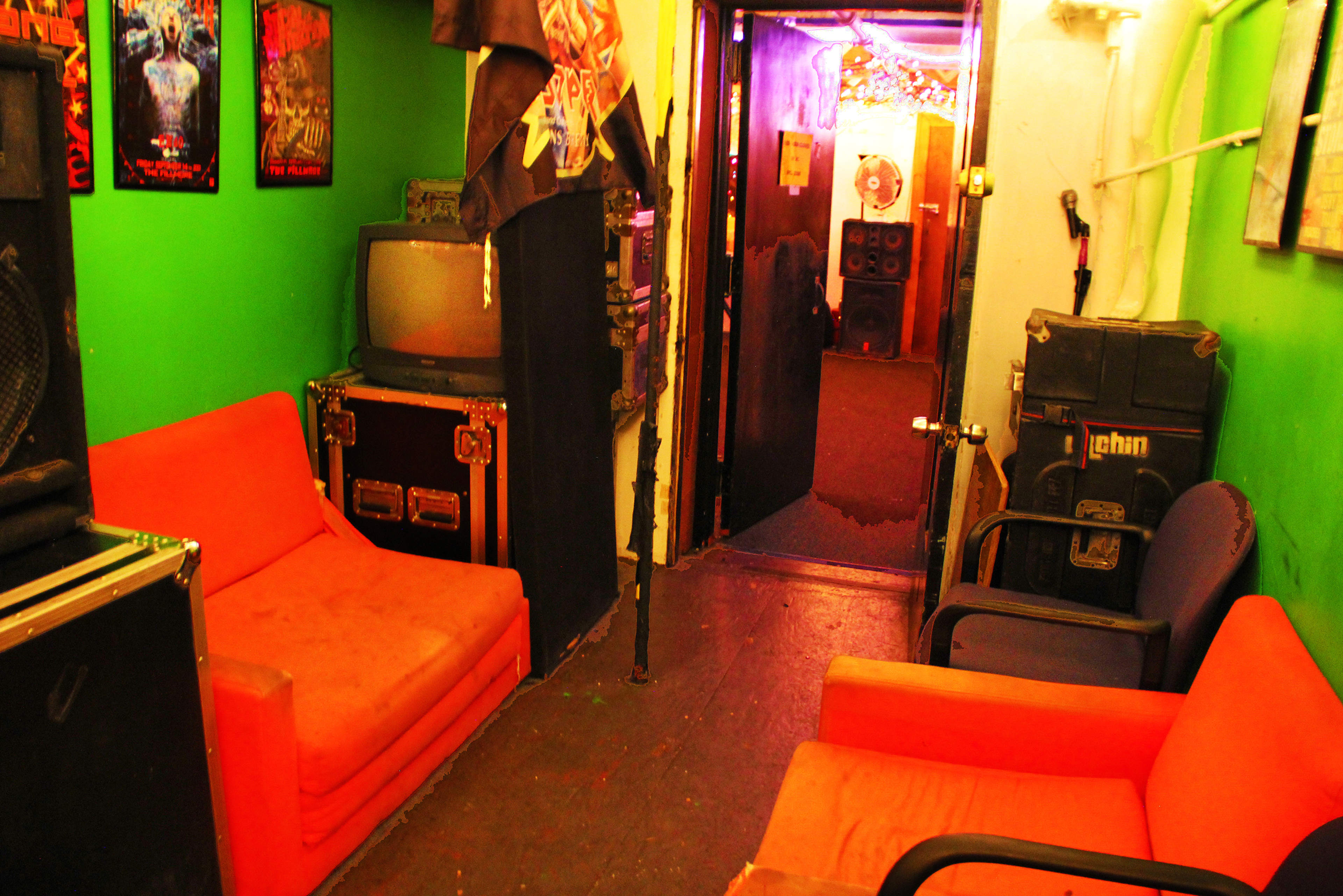 A narrow, brightly colored hallway with orange couches on either side, leading to a door at the end with dim lighting and a visible speaker system.