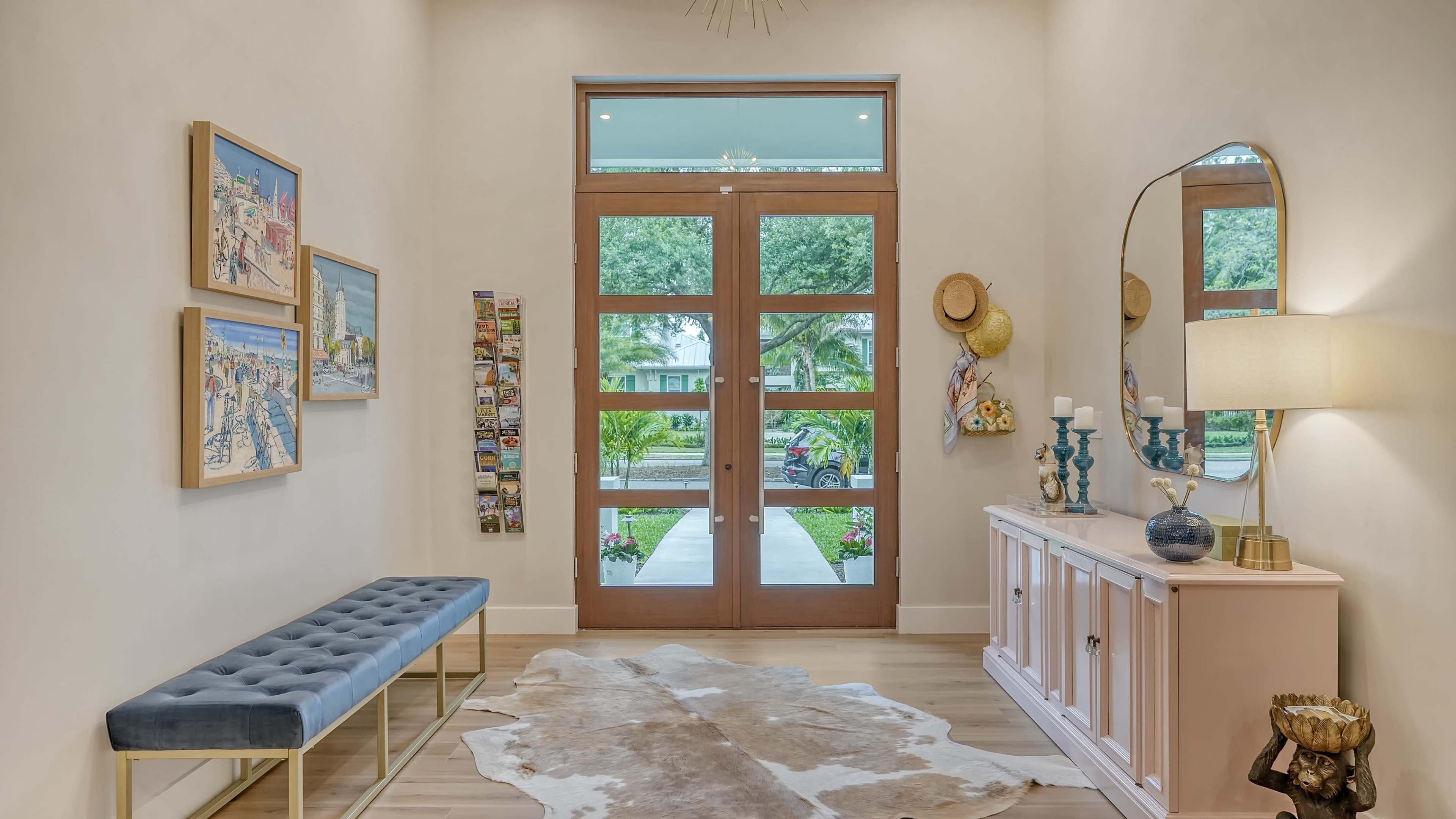 The image shows an entryway with a blue bench, a light-colored console table, a large mirror, and framed artwork on the walls.