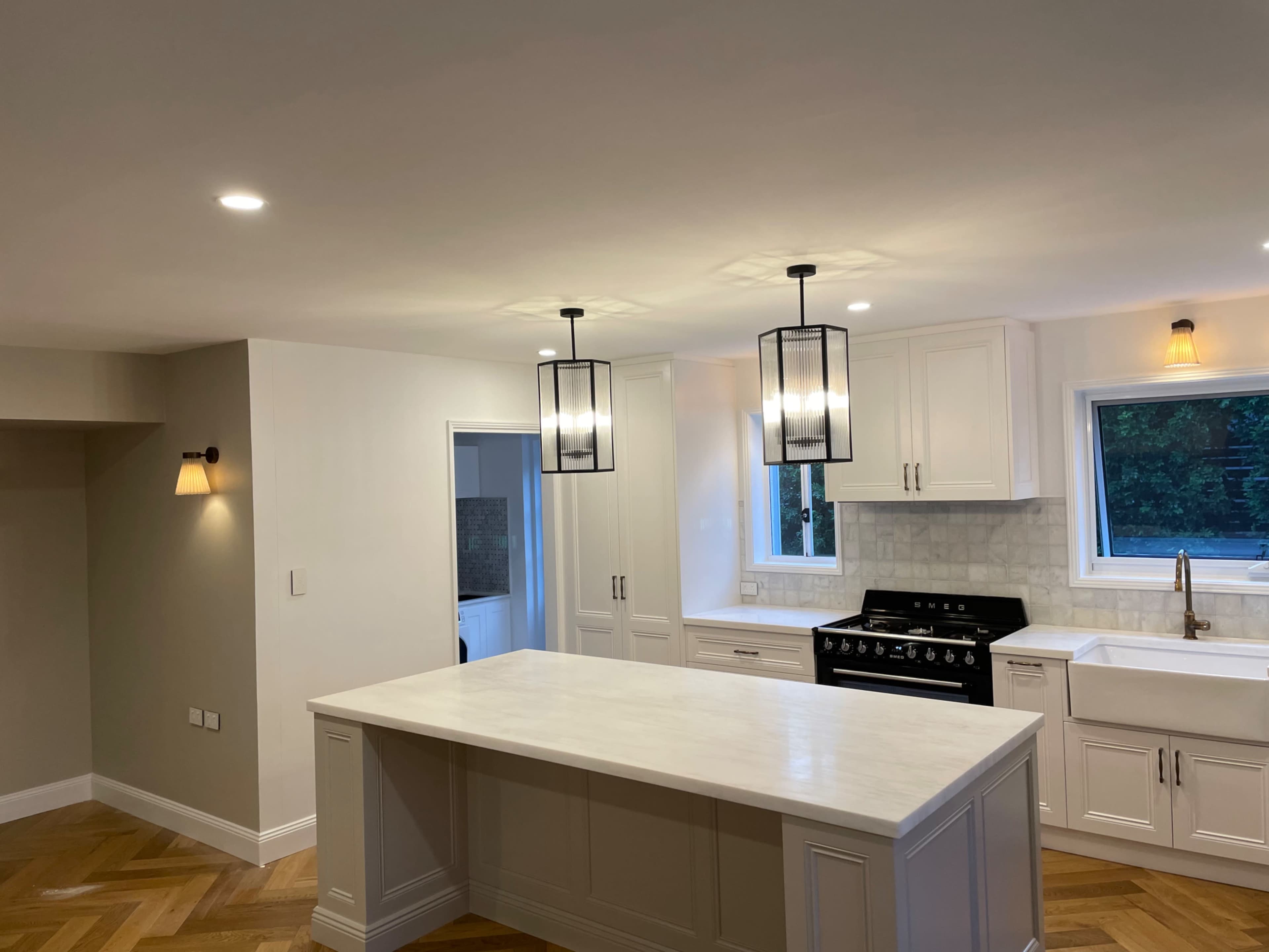 A modern kitchen featuring a central island, pendant lighting, white cabinets, and a large window above the sink.