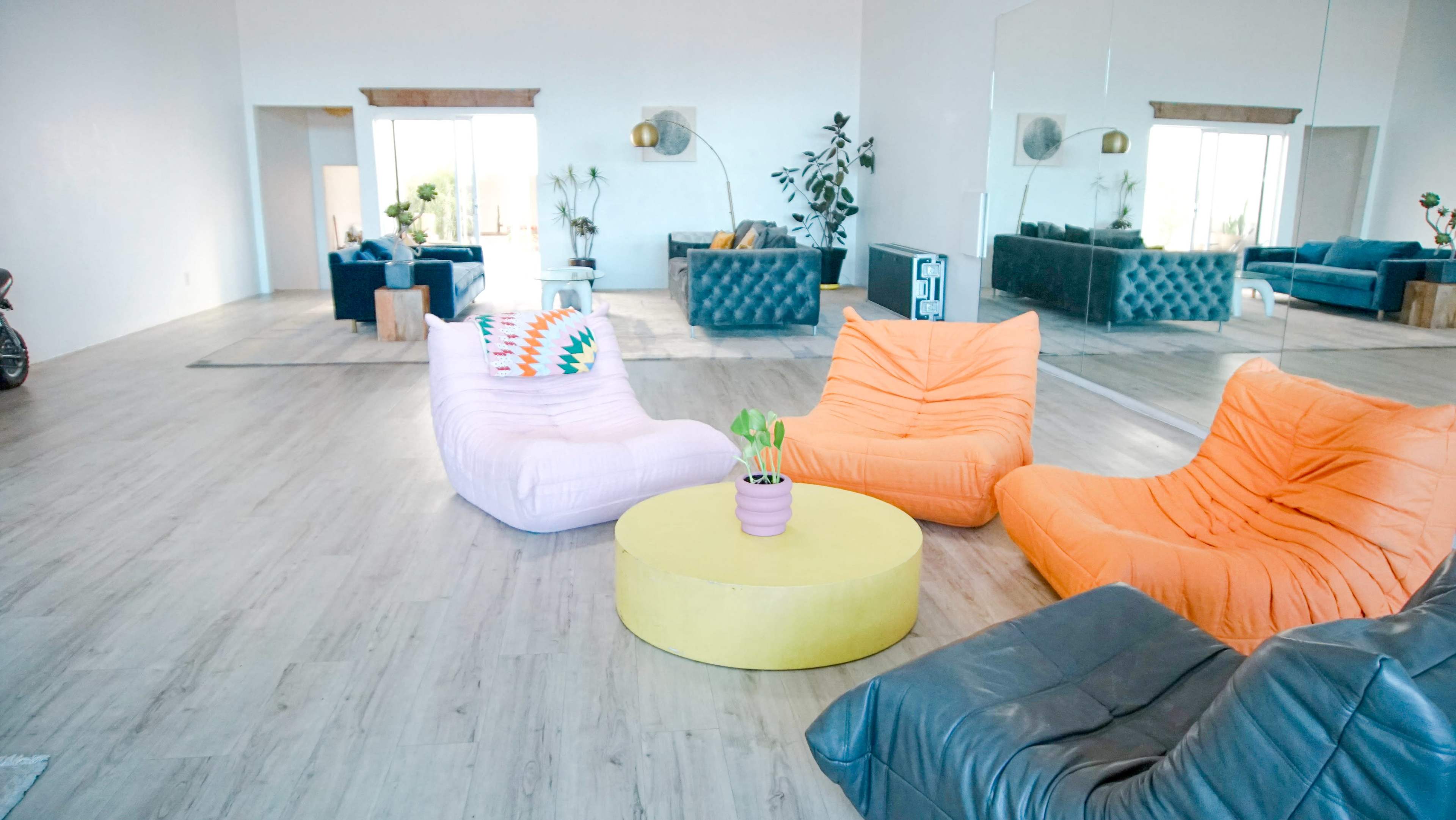 A spacious modern living room features colorful bean bag chairs and a round coffee table, surrounded by large windows and stylish furniture.