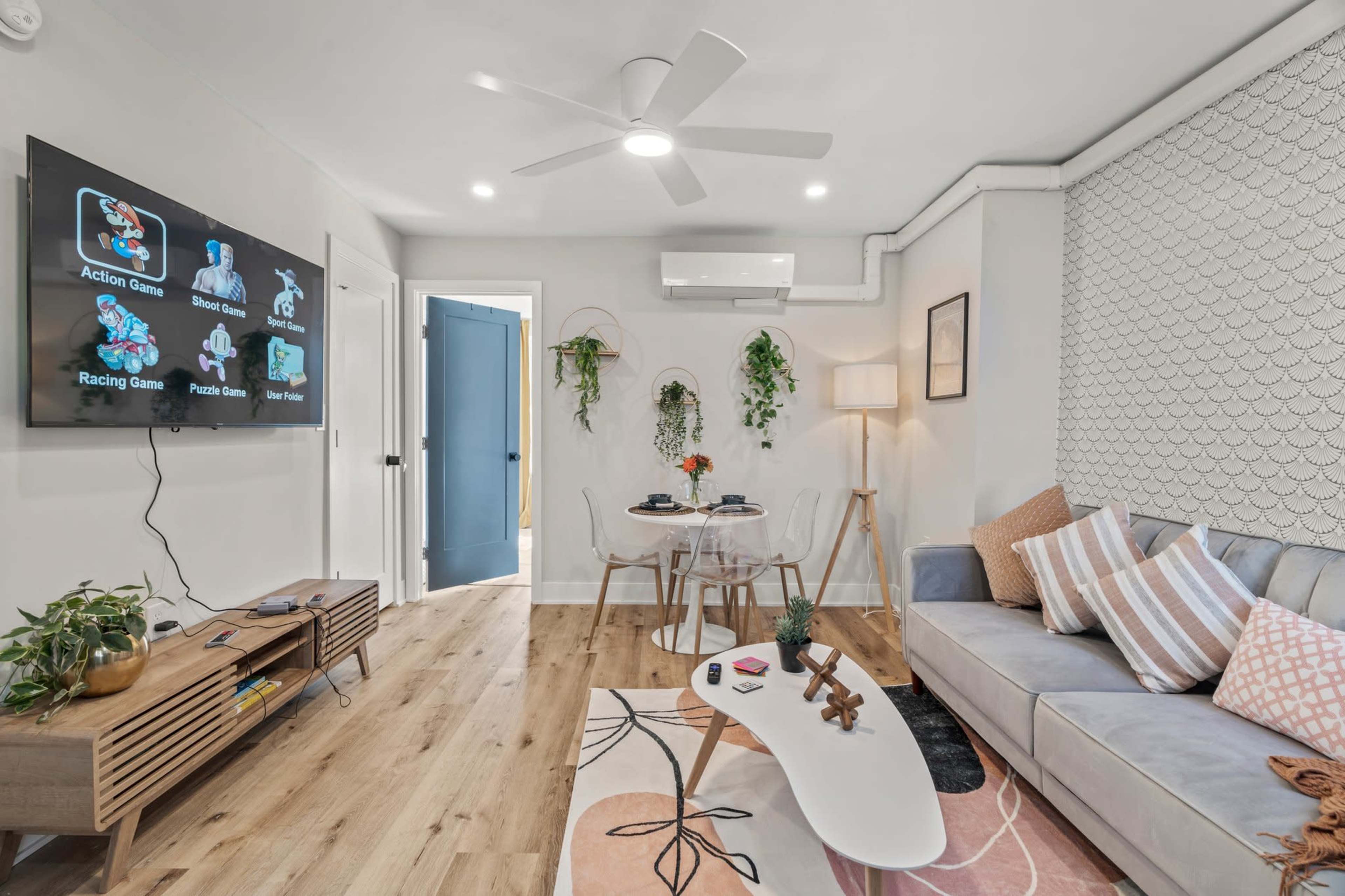 A modern living room features a gray sofa, a round coffee table, a television mounted on the wall, and indoor plants.
