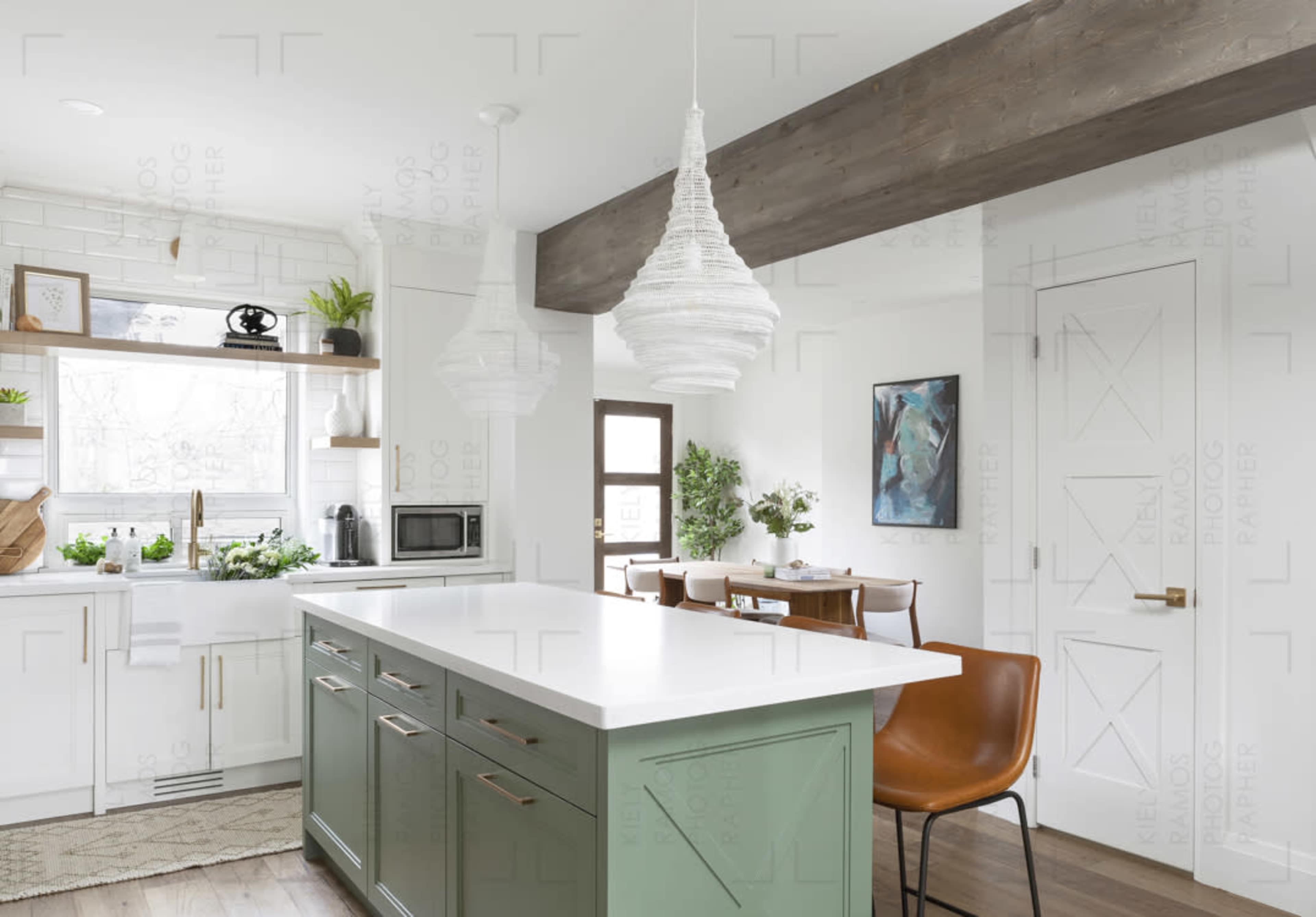 A modern kitchen with a green island, white cabinetry, and a dining area featuring brown chairs and artwork on the walls.