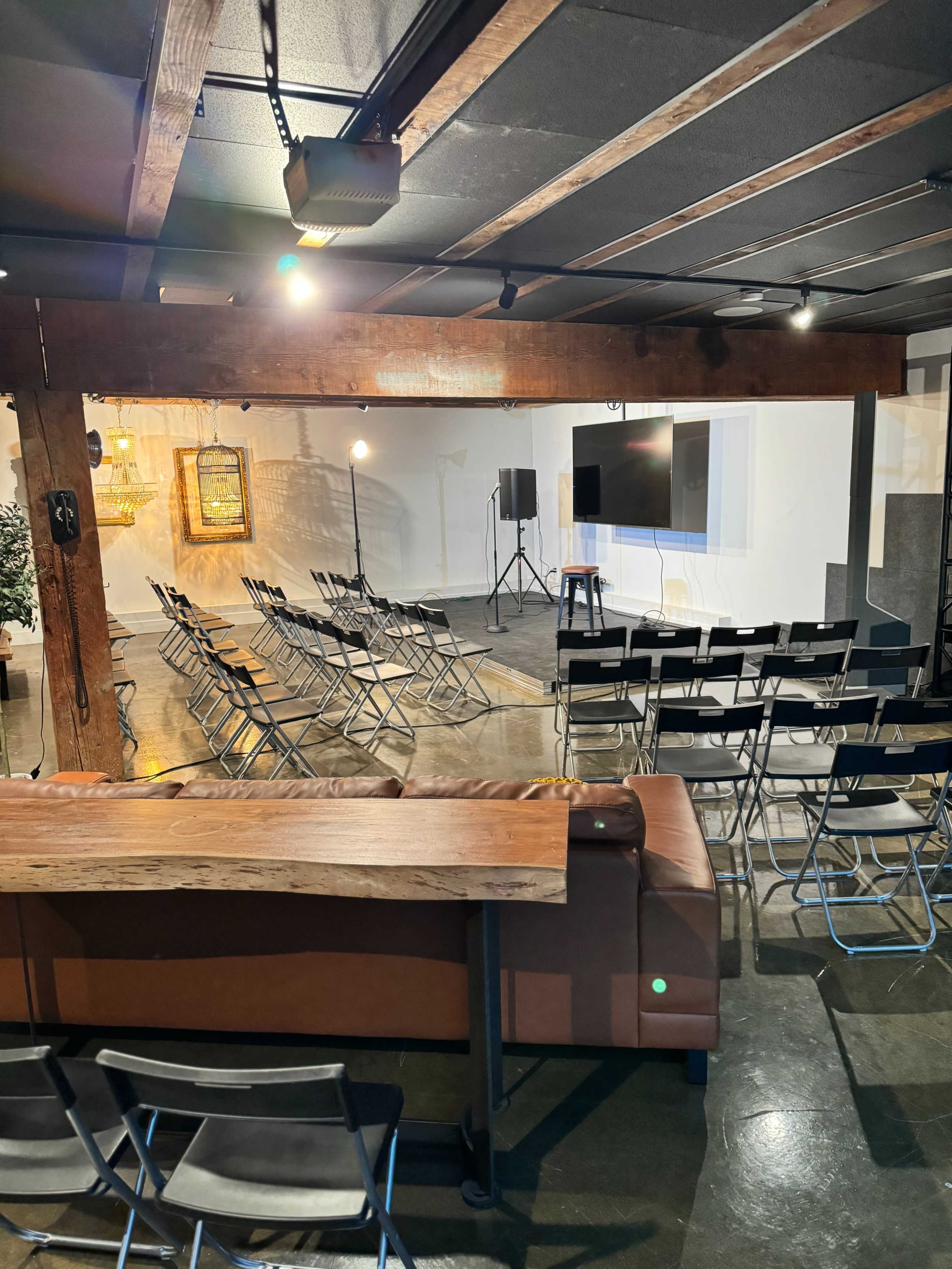 A spacious event room with rows of metal folding chairs, a large screen, and a couch positioned in the foreground.