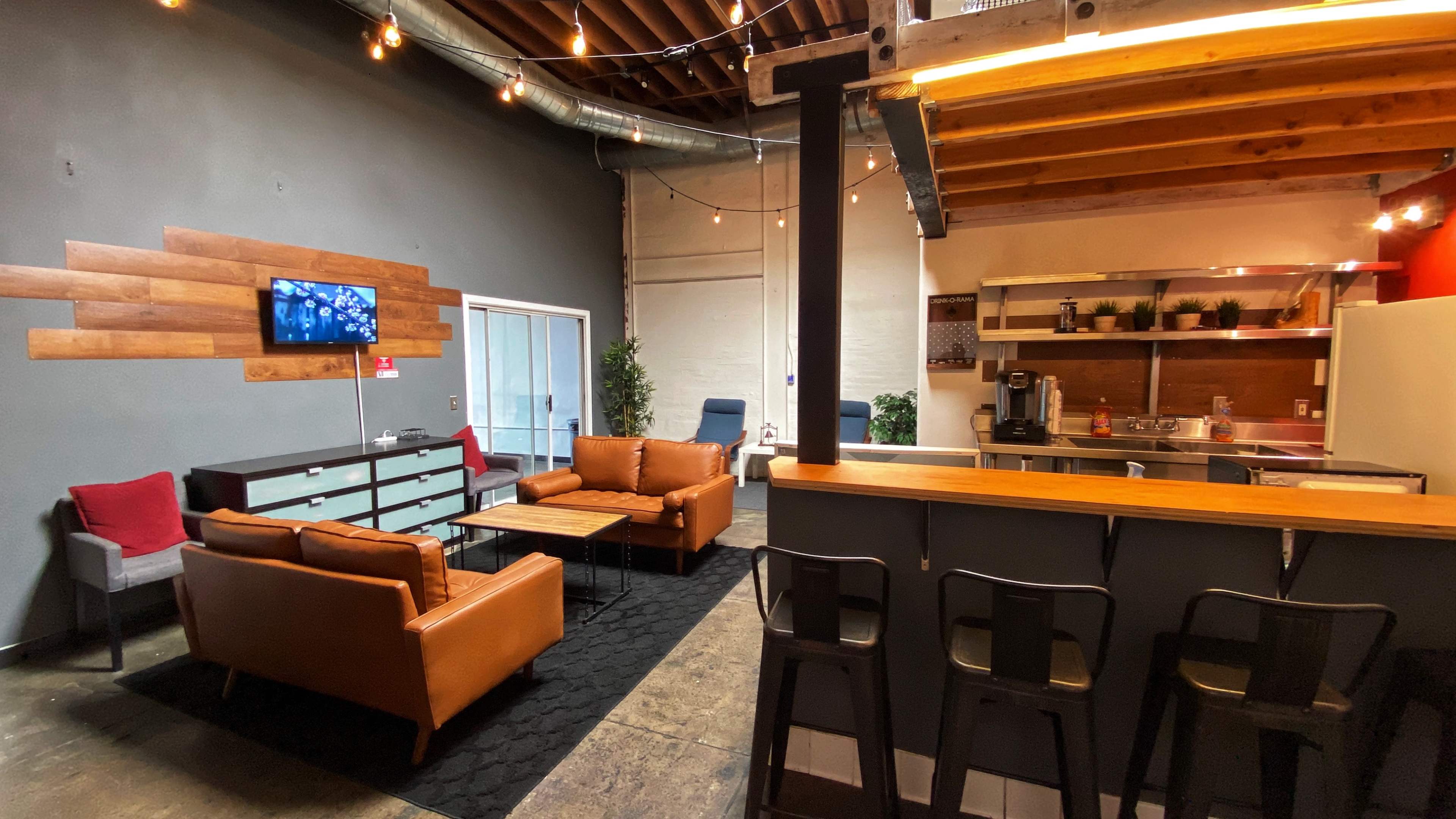 A modern lounge area features brown leather sofas, a wooden coffee table, and a kitchenette with bar seating.