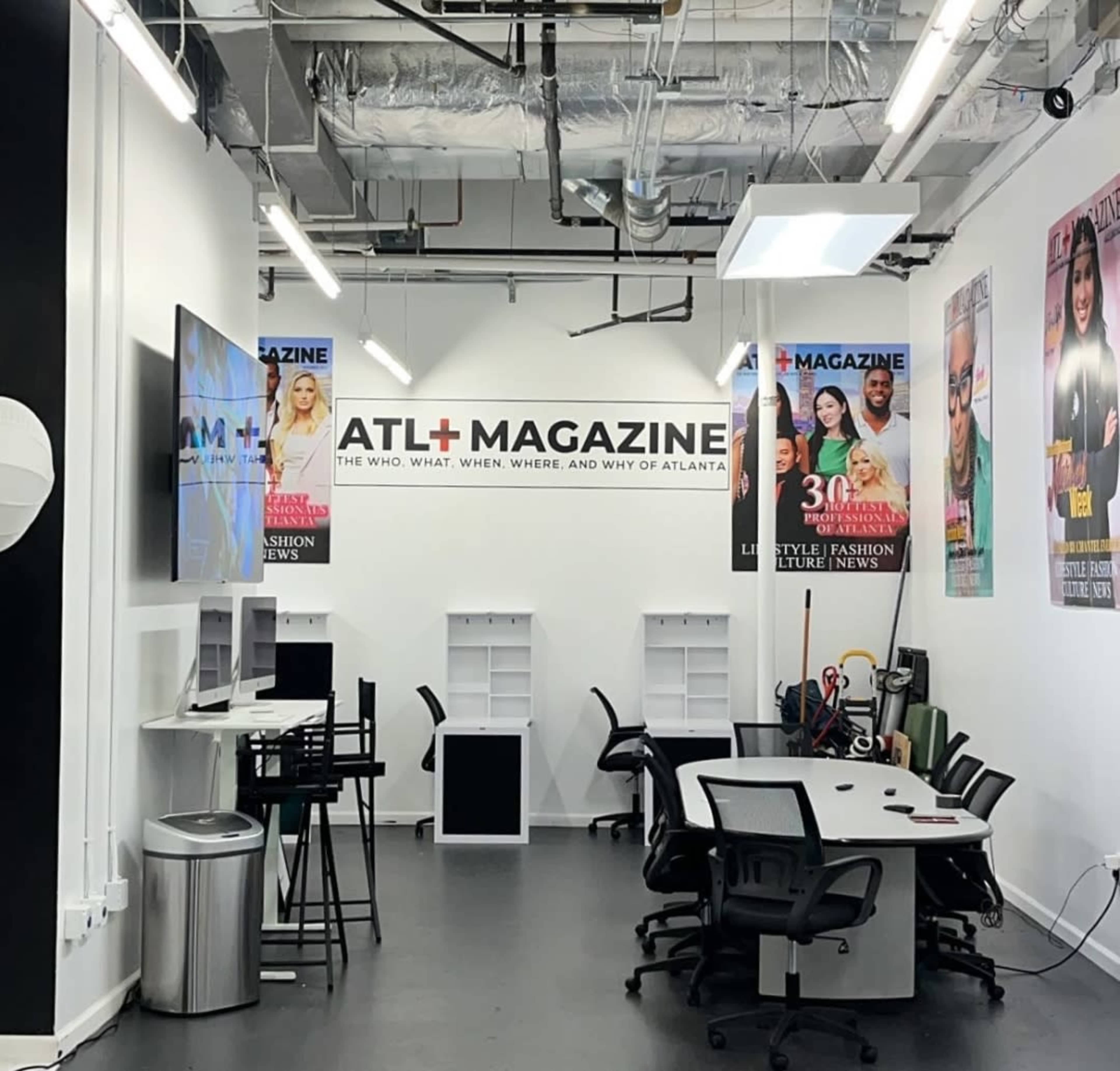 The image shows a modern office space with a conference table, black chairs, and promotional magazine covers displayed on the walls.