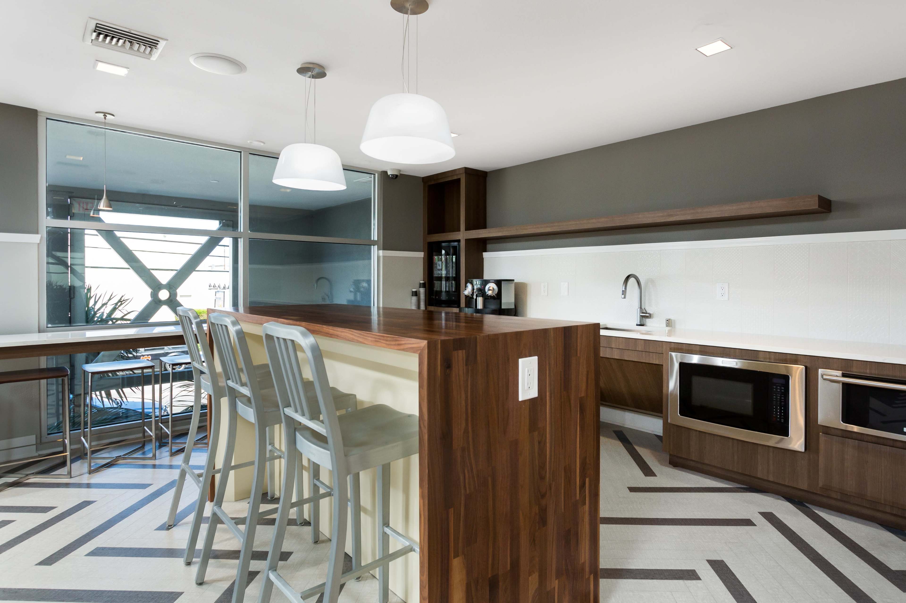 A modern kitchen with a wooden island featuring bar stools, stainless steel appliances, and a large window illuminating the space.
