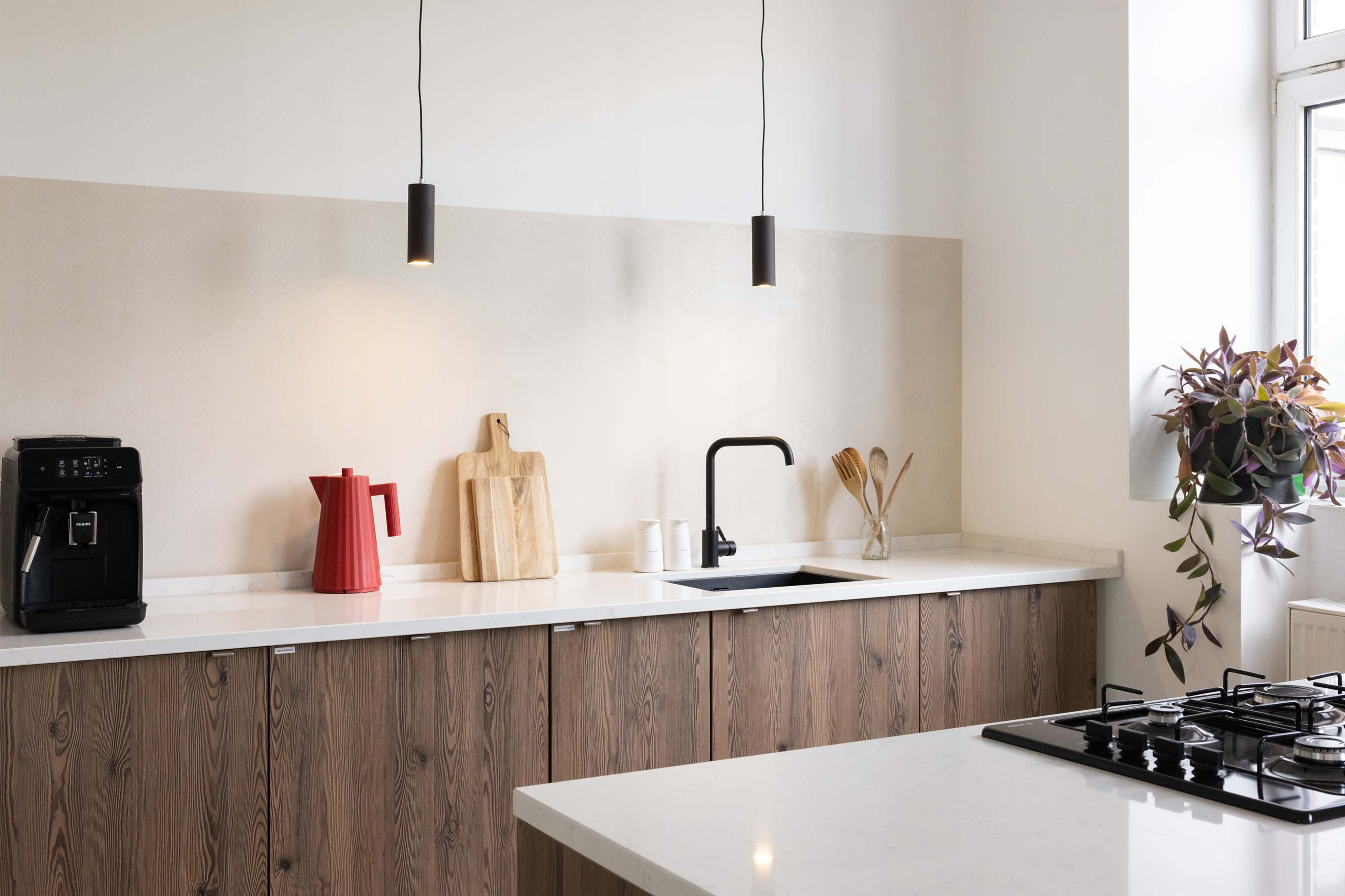 A modern kitchen features wooden cabinetry, a white countertop, a black sink, and pendant lighting above the workspace.