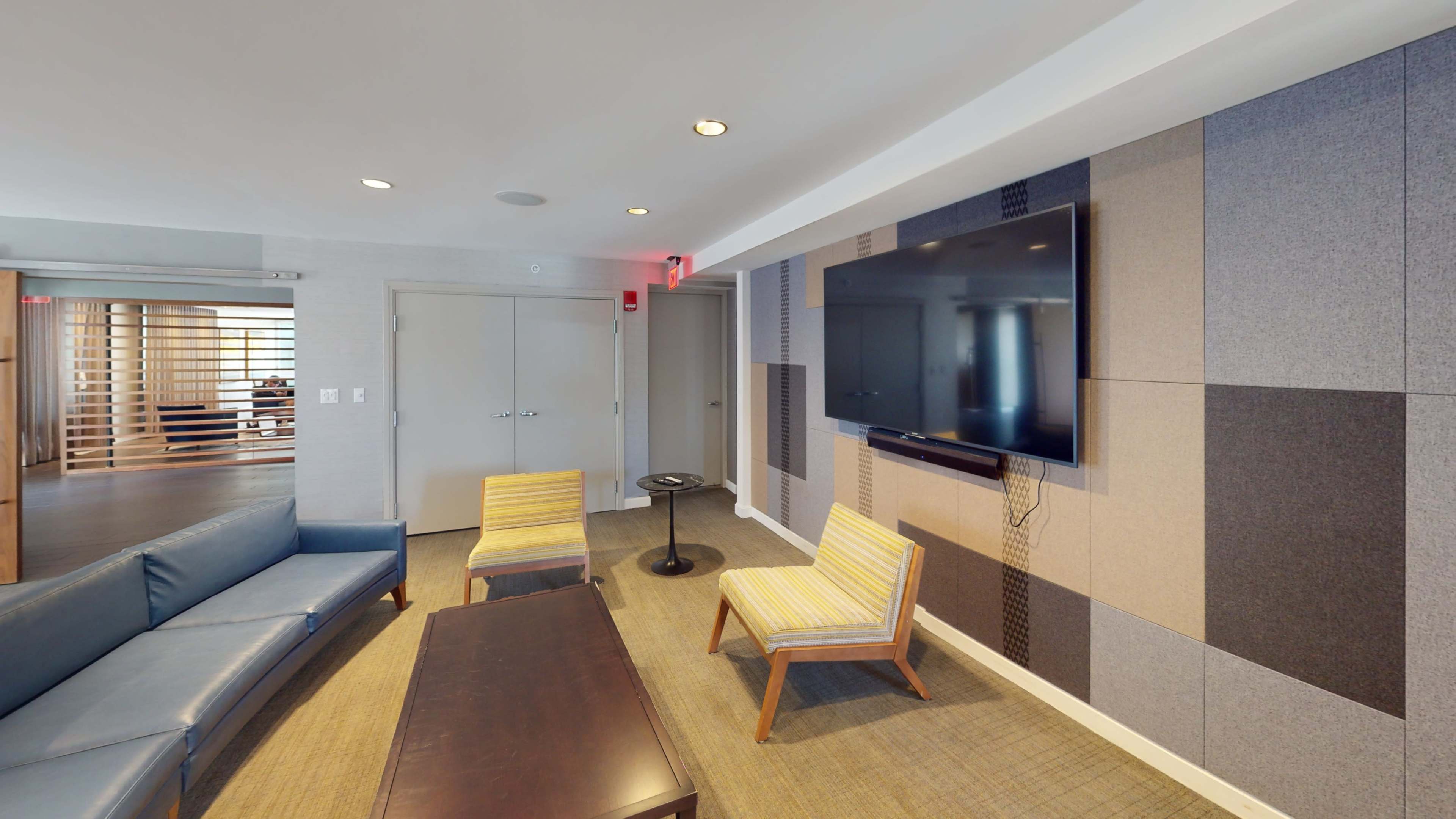 The image shows a modern lounge area with a blue sofa, two striped chairs, a dark coffee table, and a wall-mounted television.