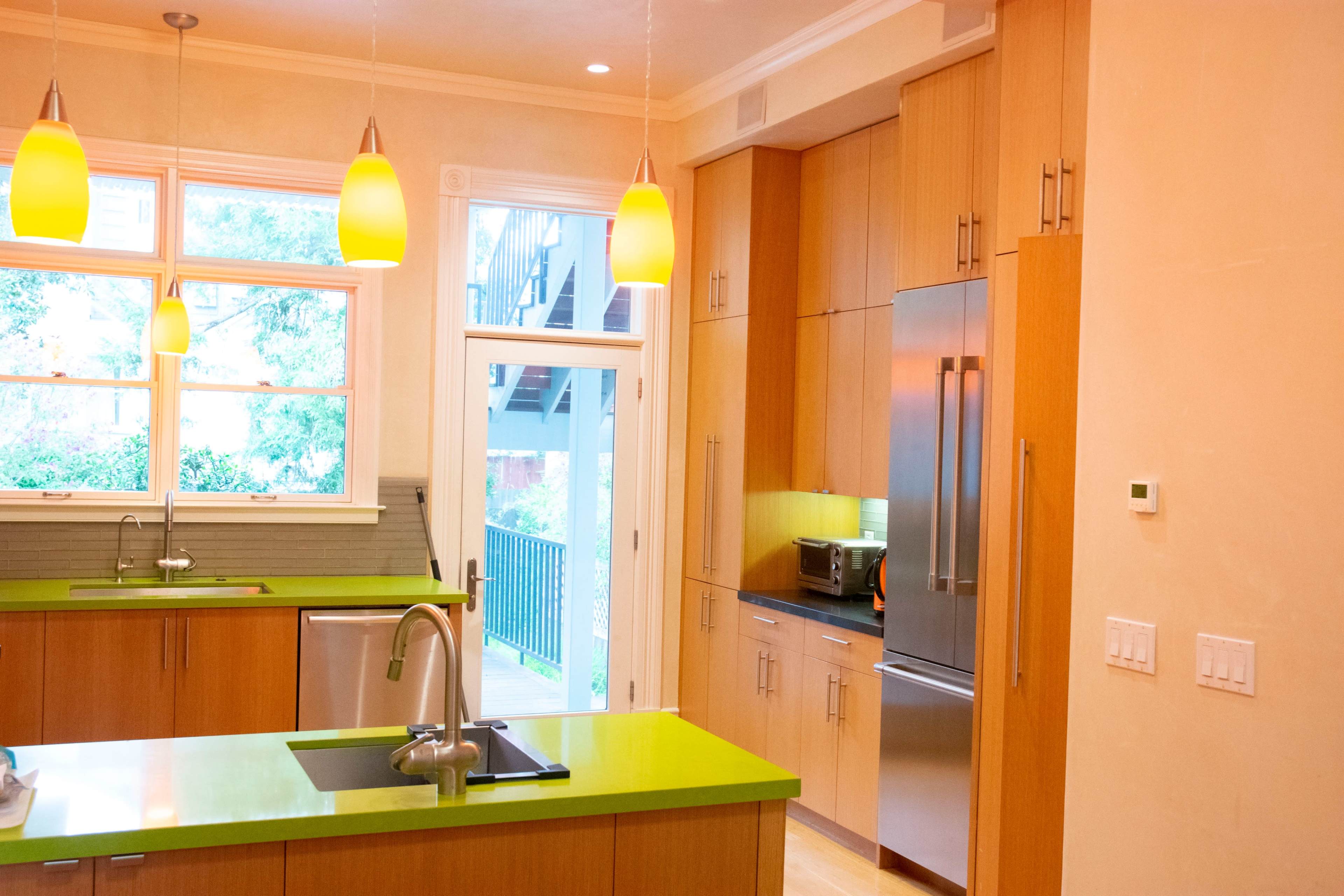 The kitchen features wooden cabinets, stainless steel appliances, and a bright green countertop with pendant lighting overhead.